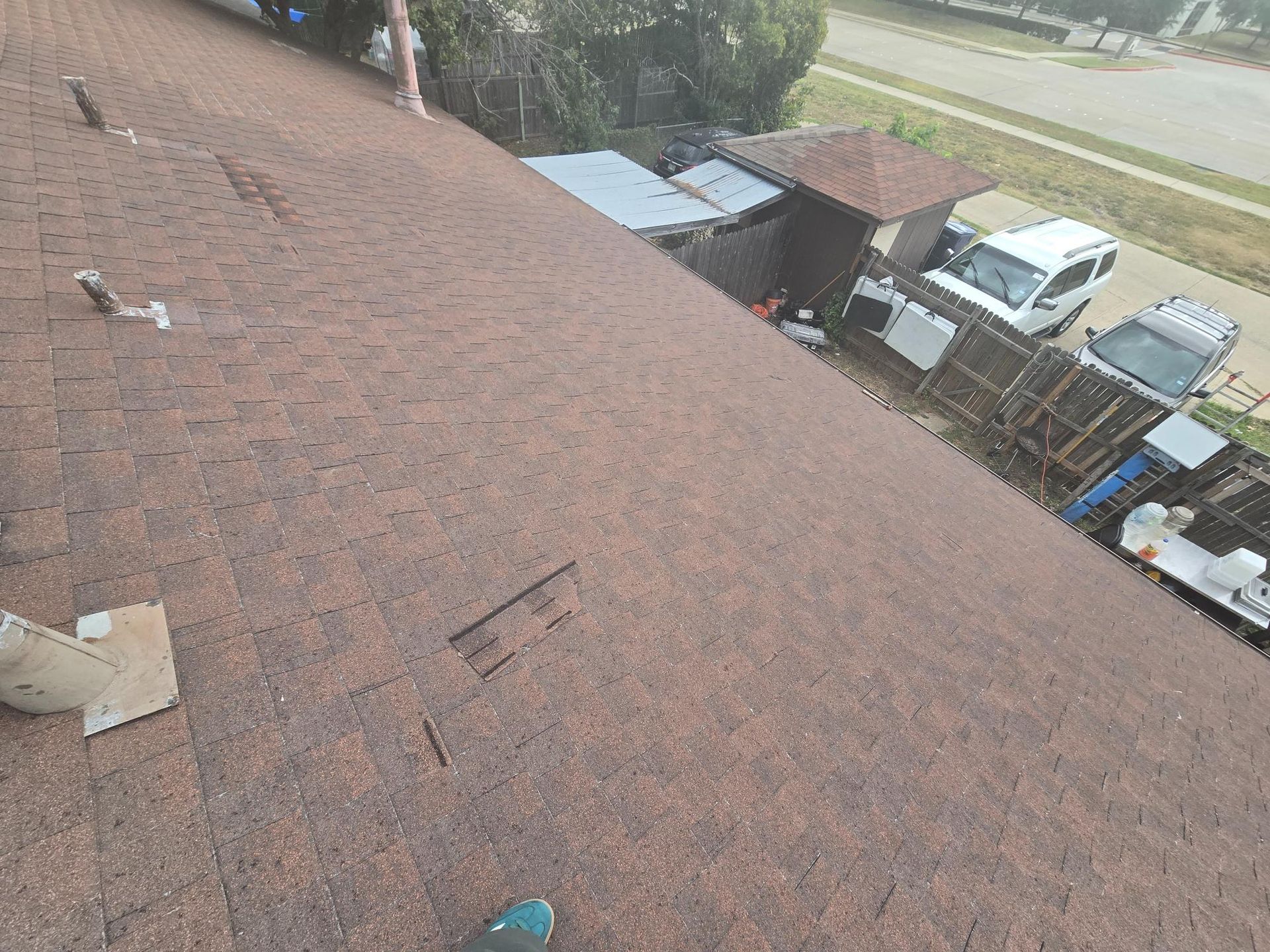 View from a rooftop, looking at brown asphalt shingles, with buildings and a street in the background.