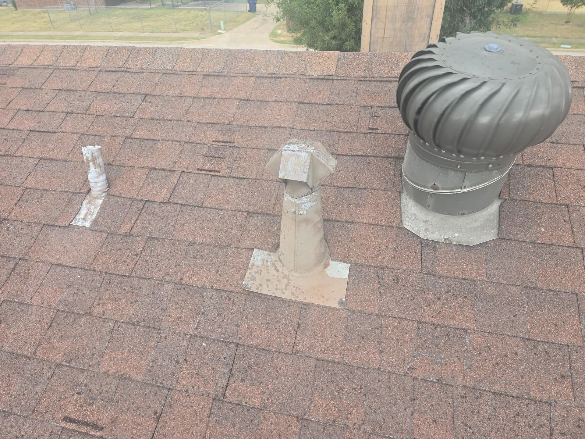 Brown shingled rooftop with three vents: a broken pipe, a metal vent, and a turbine.