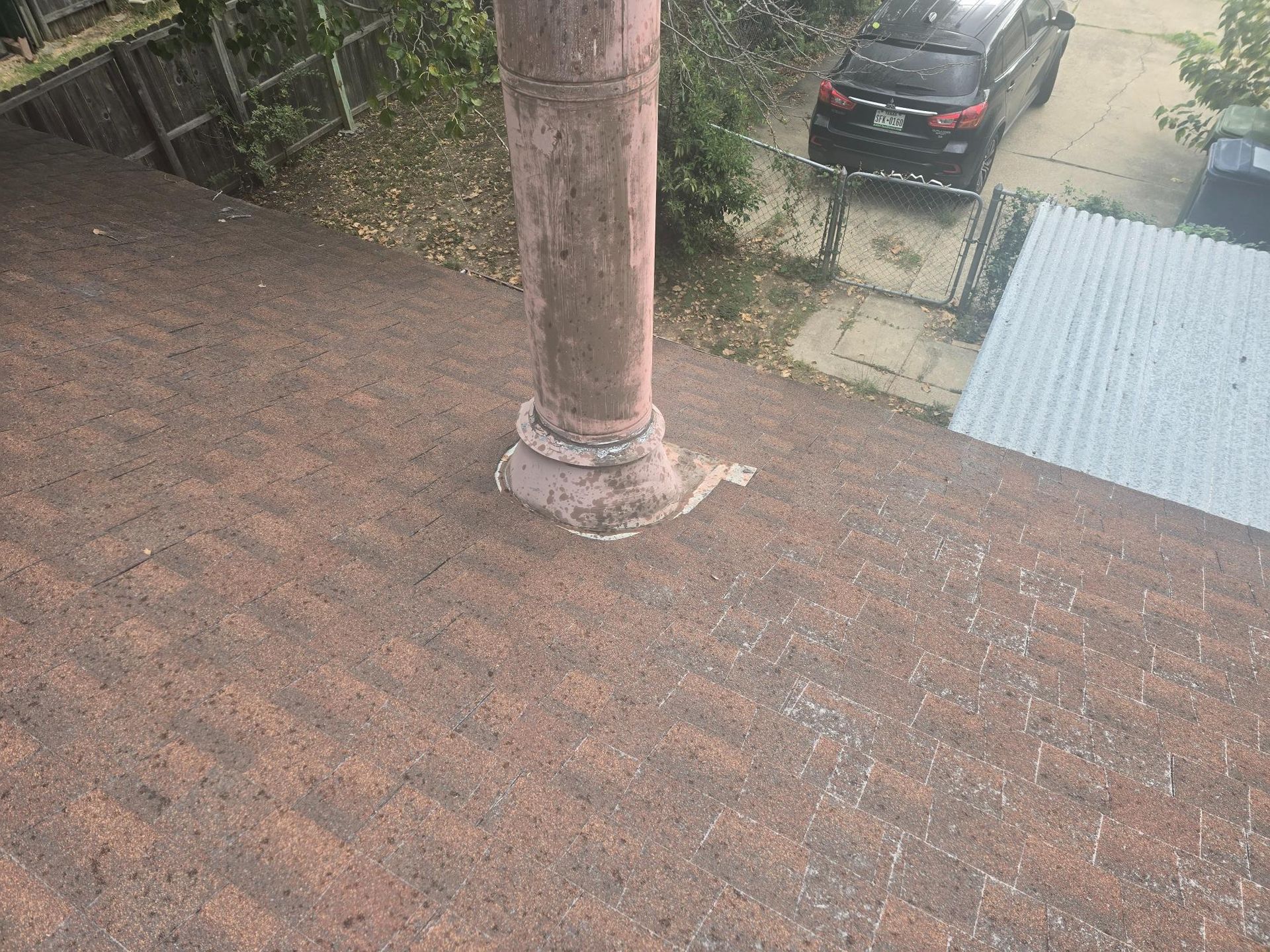 Roof with brown shingles, chimney, and a parked black car.