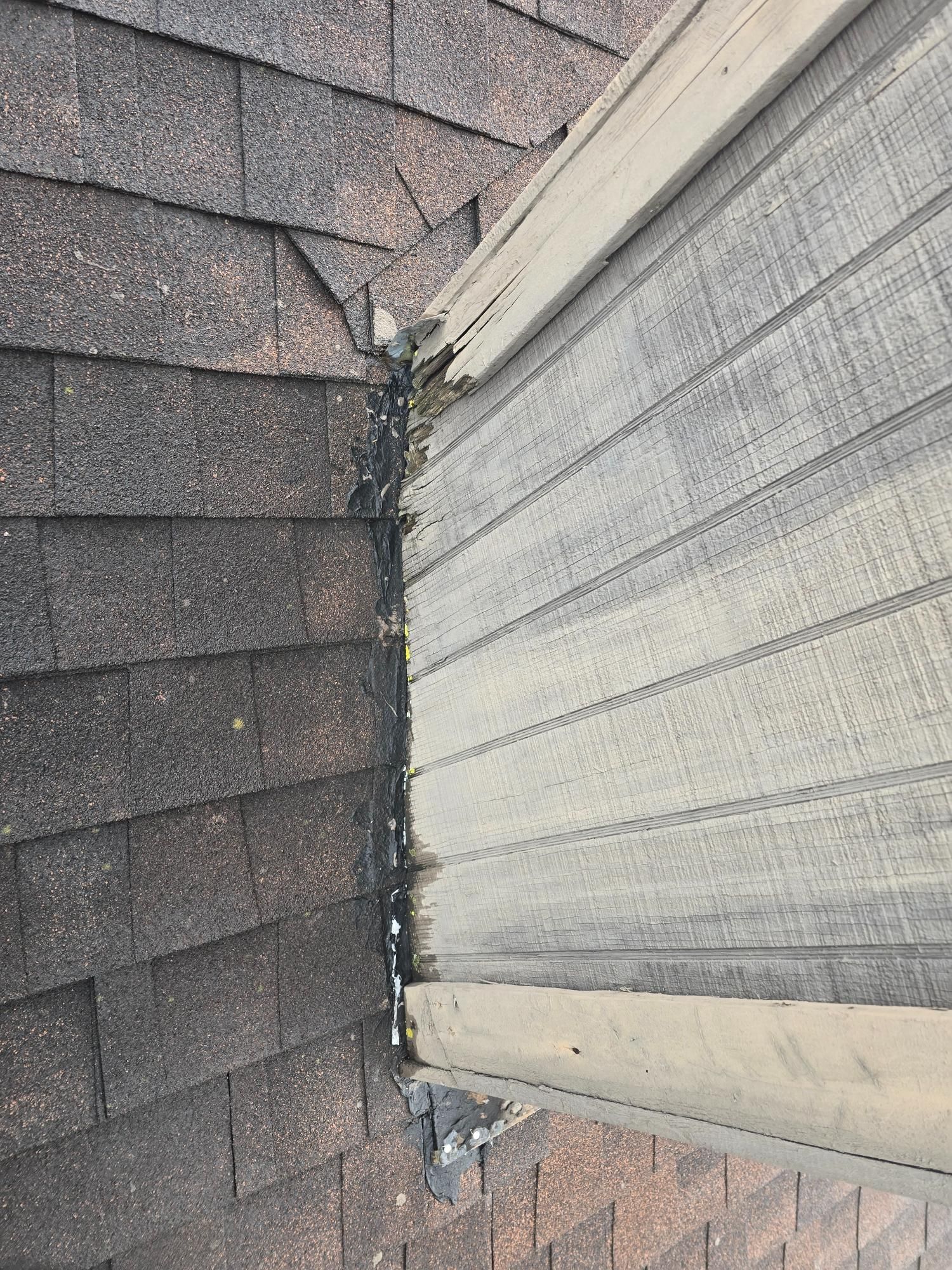 Roofing shingles meet siding, with damaged wood and sealant visible.
