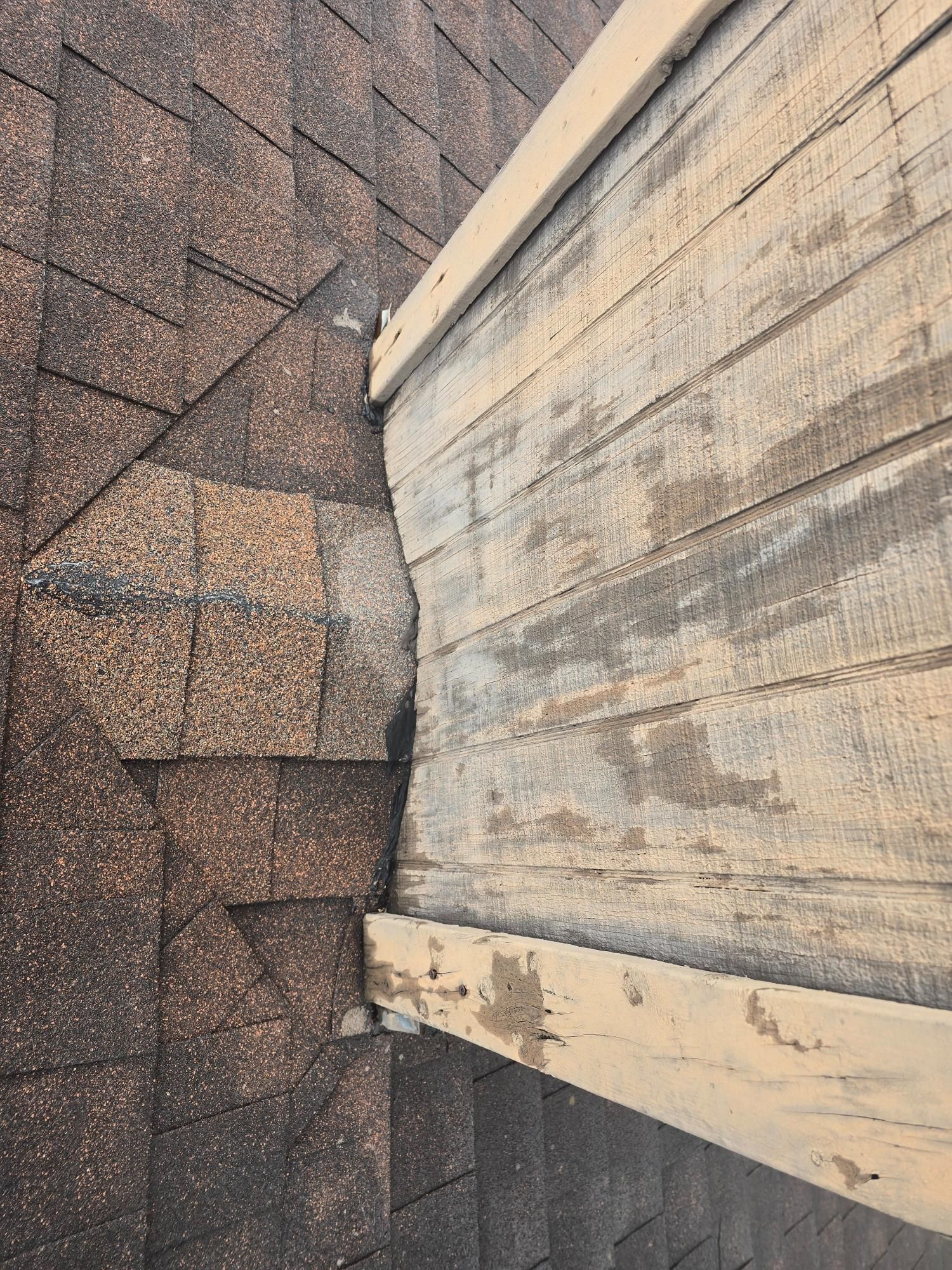 Close-up of brown roof shingles next to weathered wooden fascia board with a dark stain at the edge.