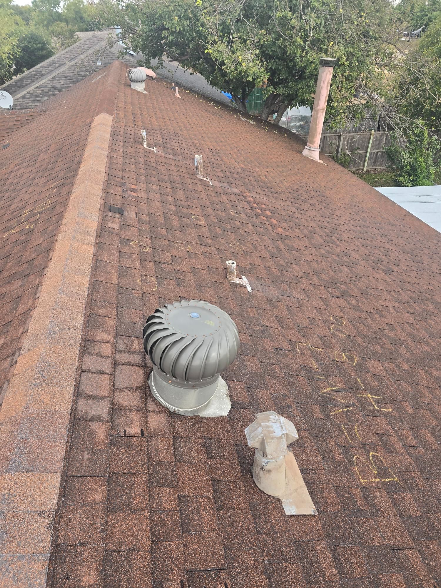 Brown shingle roof with vents and a spinning turbine in an outdoor setting.
