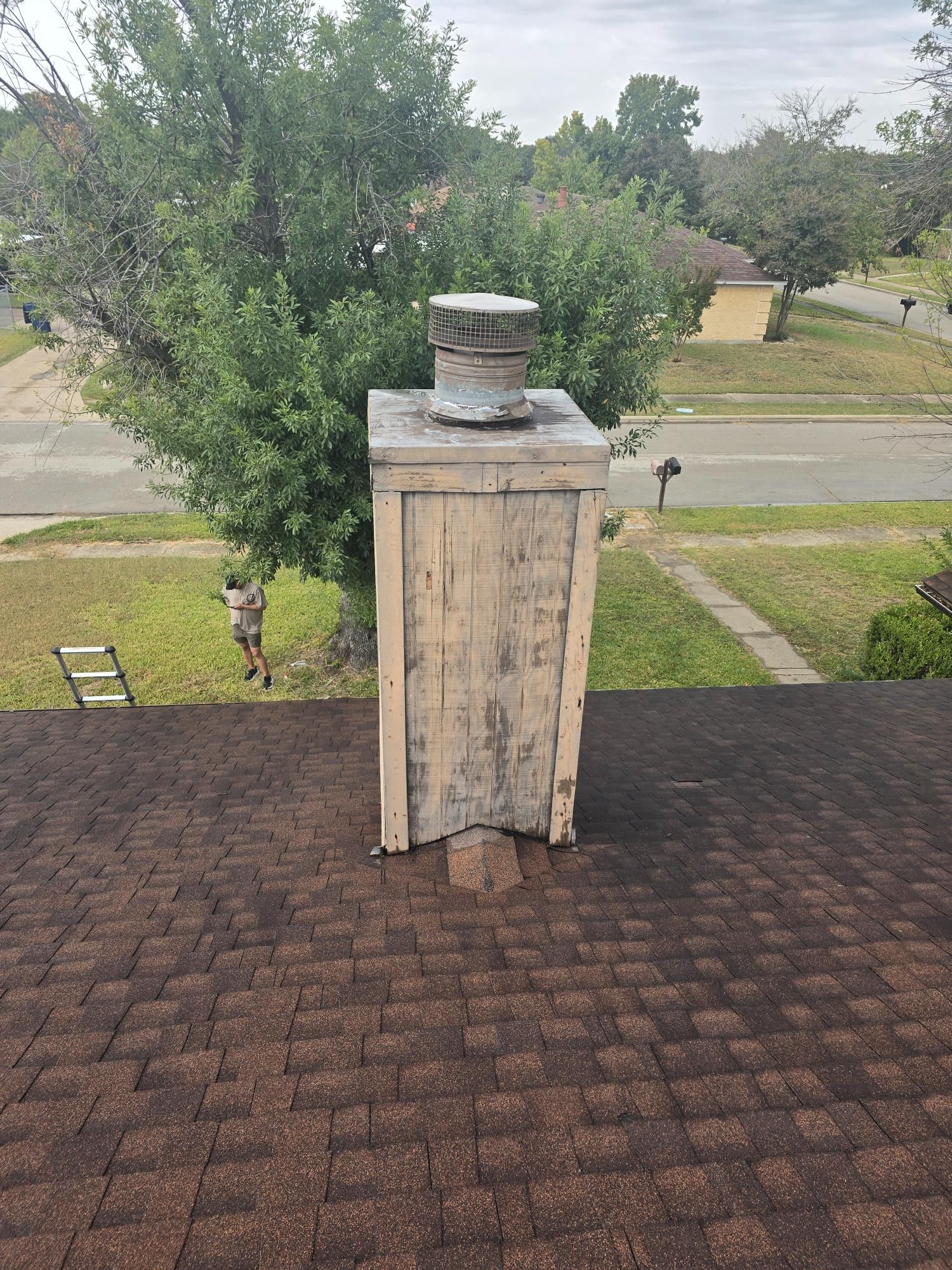 Chimney on a roof; weathered wood and a metal cap; asphalt shingles.
