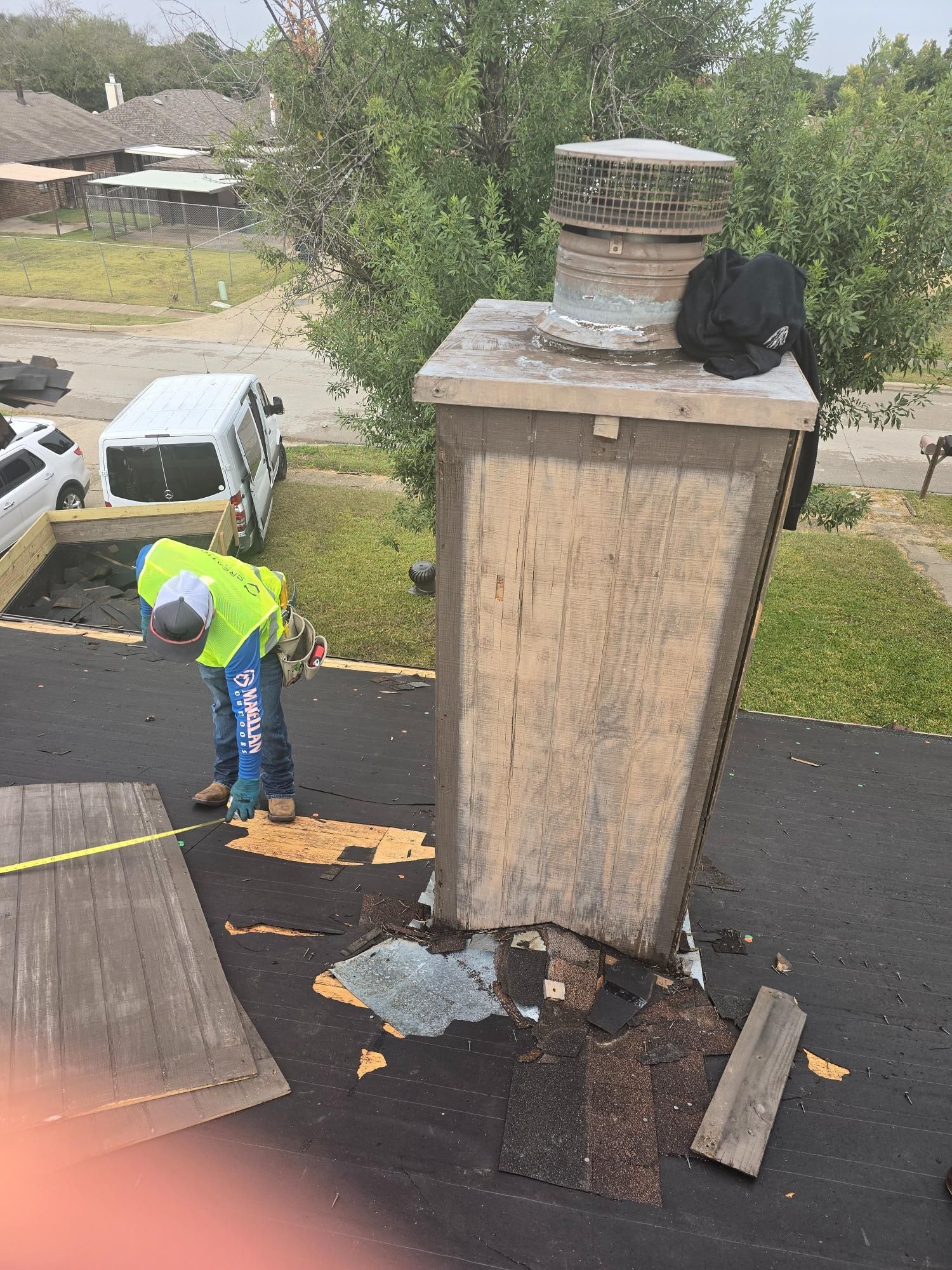 Person on a roof inspecting a chimney. The chimney is weathered, and roof shingles are damaged.