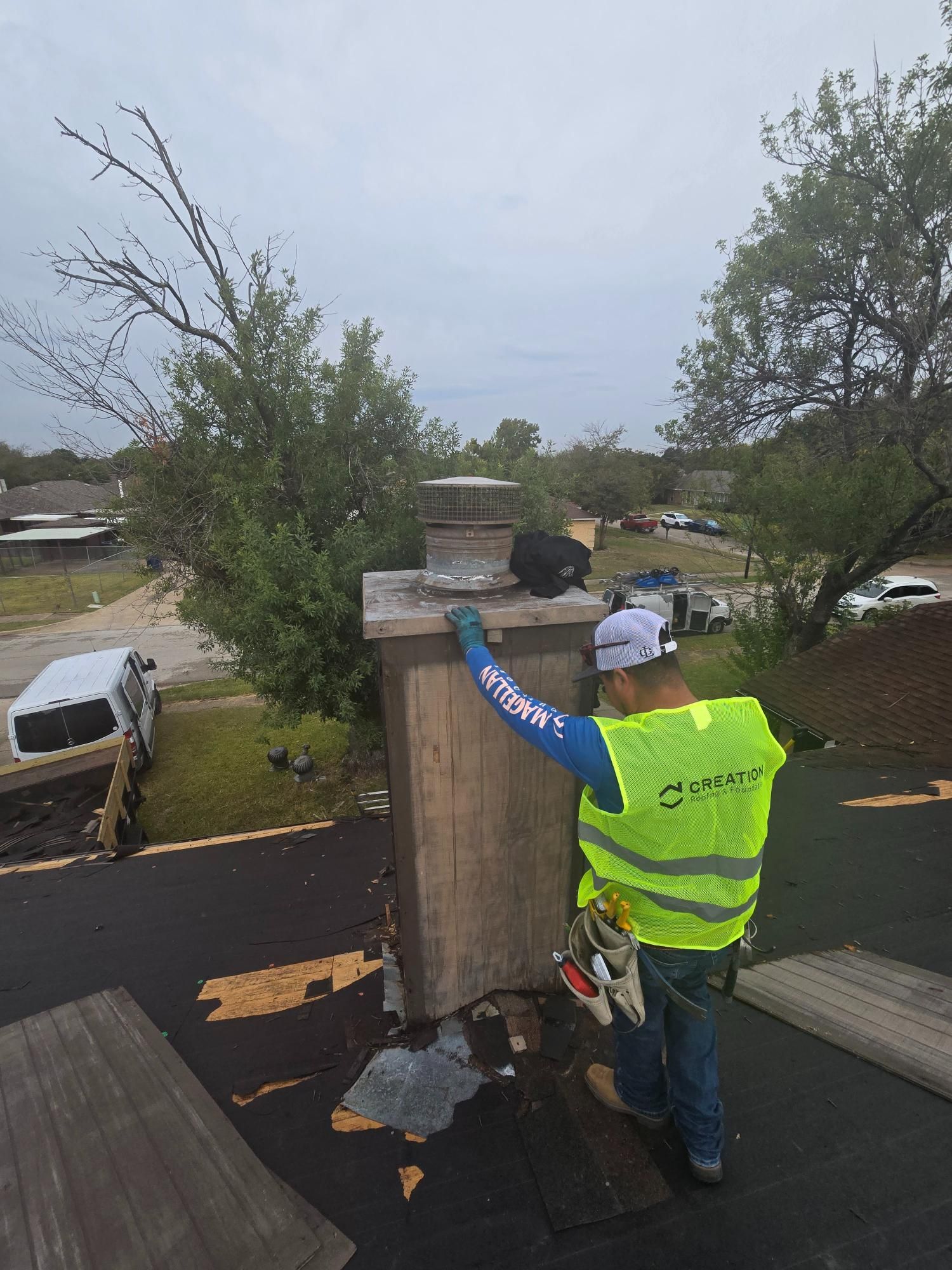 Roofer in safety vest inspecting a chimney on a residential roof, overcast sky.