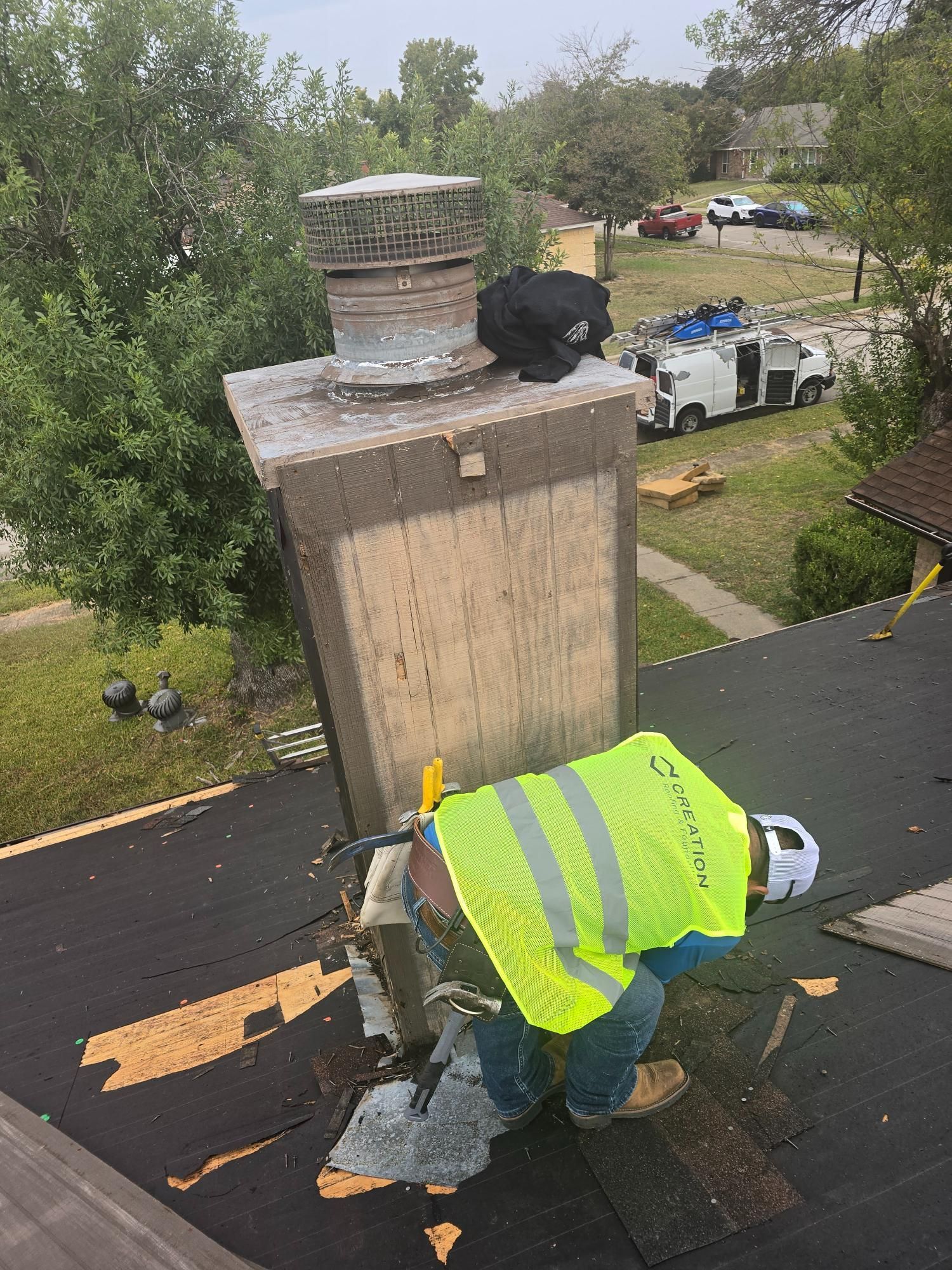 Roofer, wearing a safety vest and helmet, repairs chimney on a roof.
