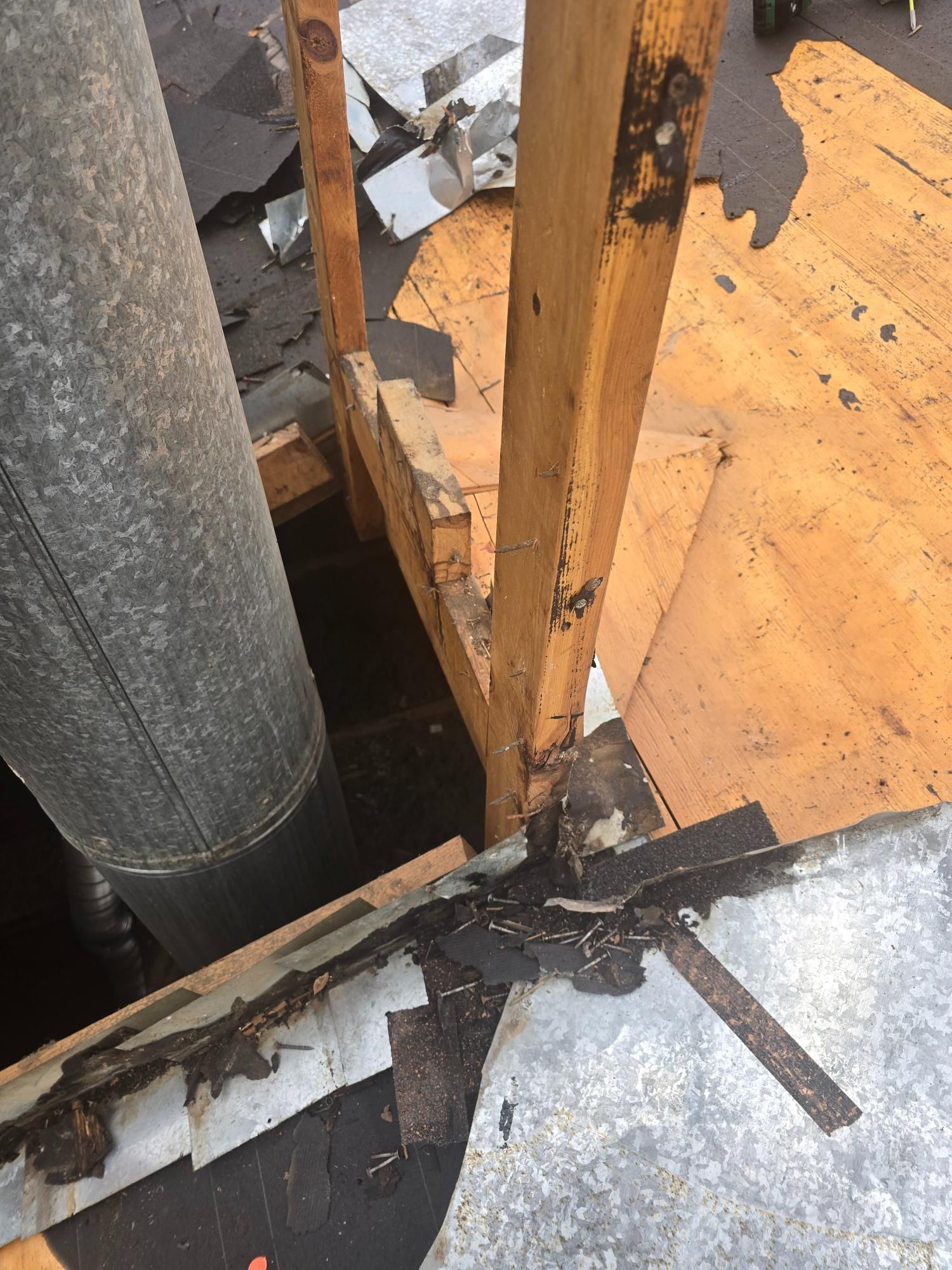 Wooden structure on roof surrounding a metal chimney, with torn roofing materials scattered.
