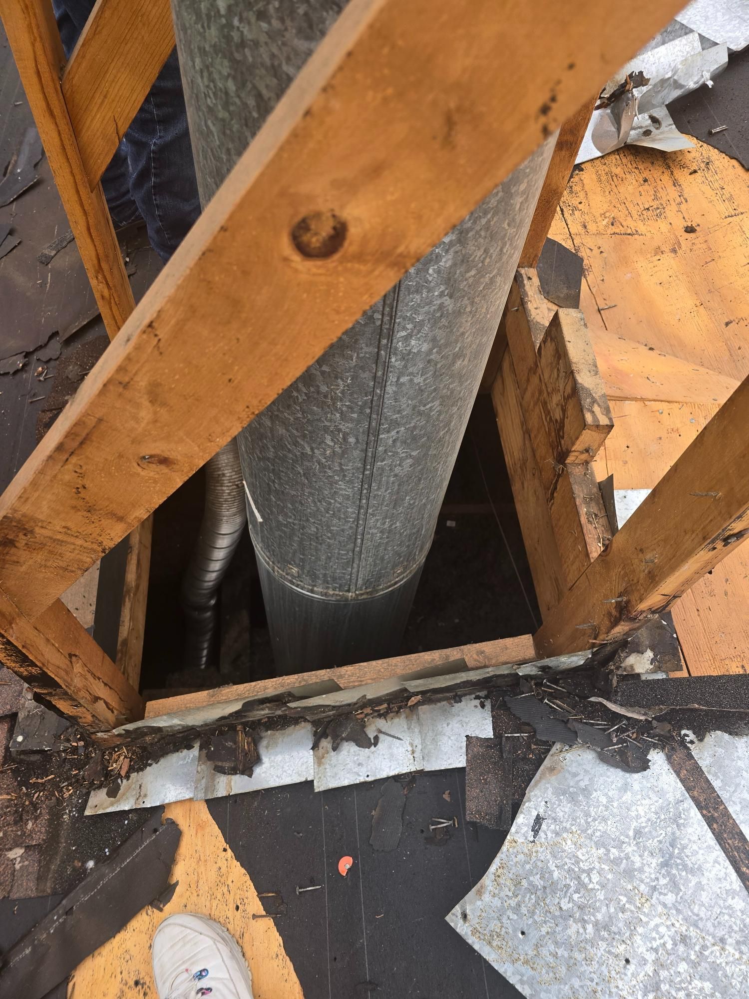 Wooden frame around a metal chimney on a roof with visible damage and debris.