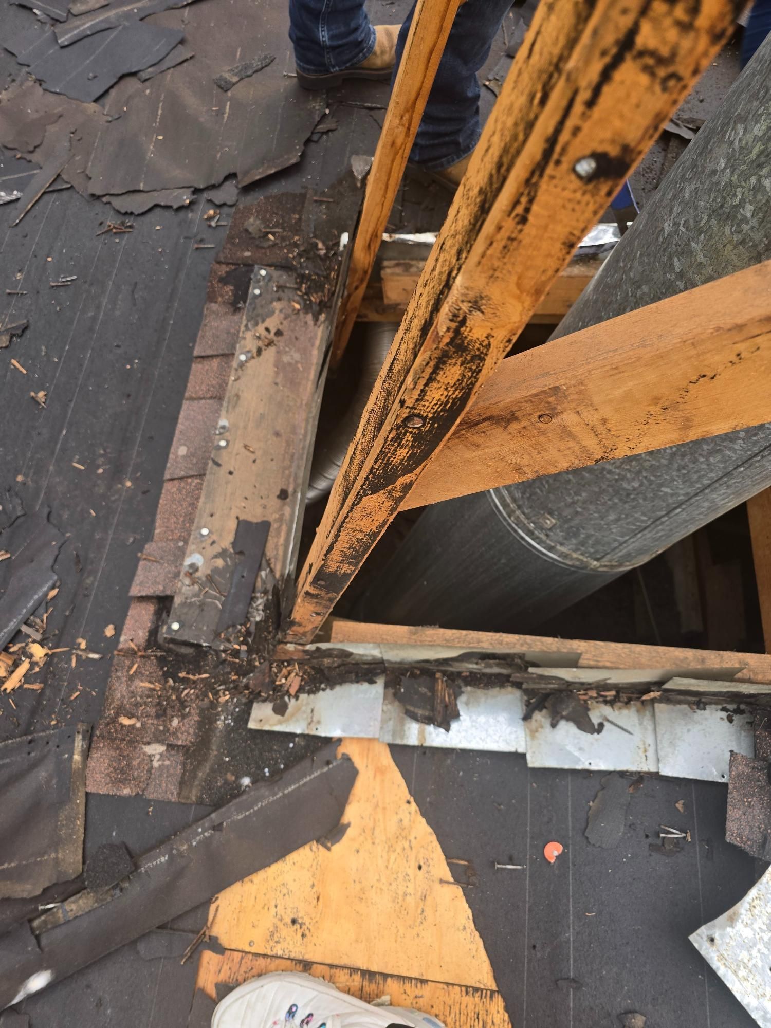 View from above a roof with exposed wooden beams, a brick chimney, and roofing materials being worked on.
