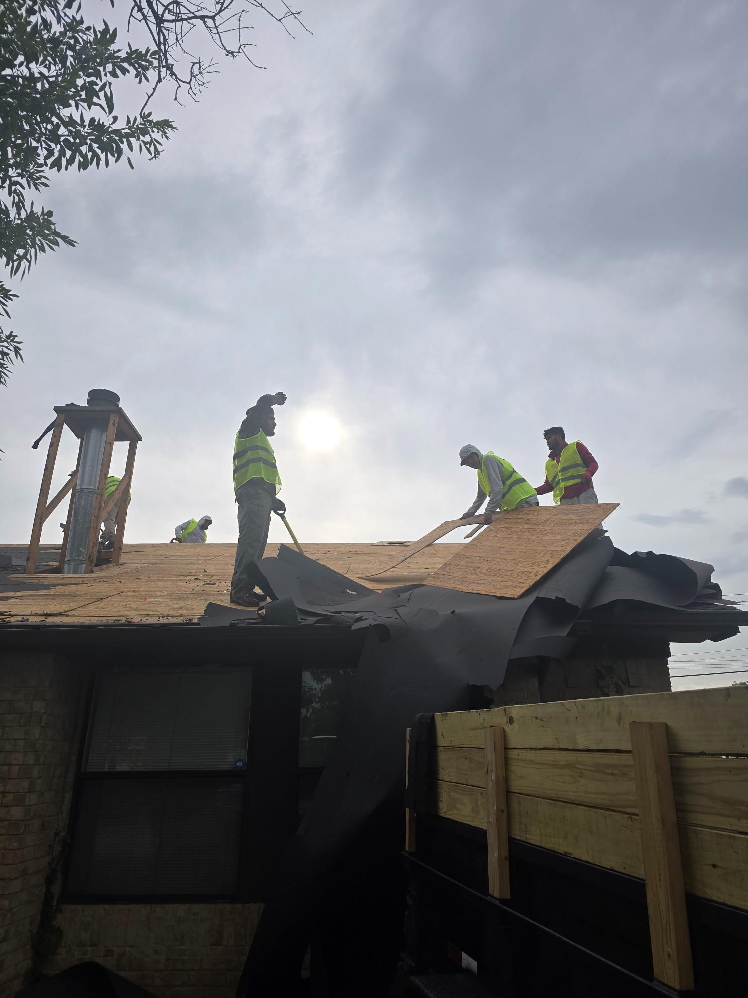 Roofers in safety vests working on a roof, cloudy sky overhead.