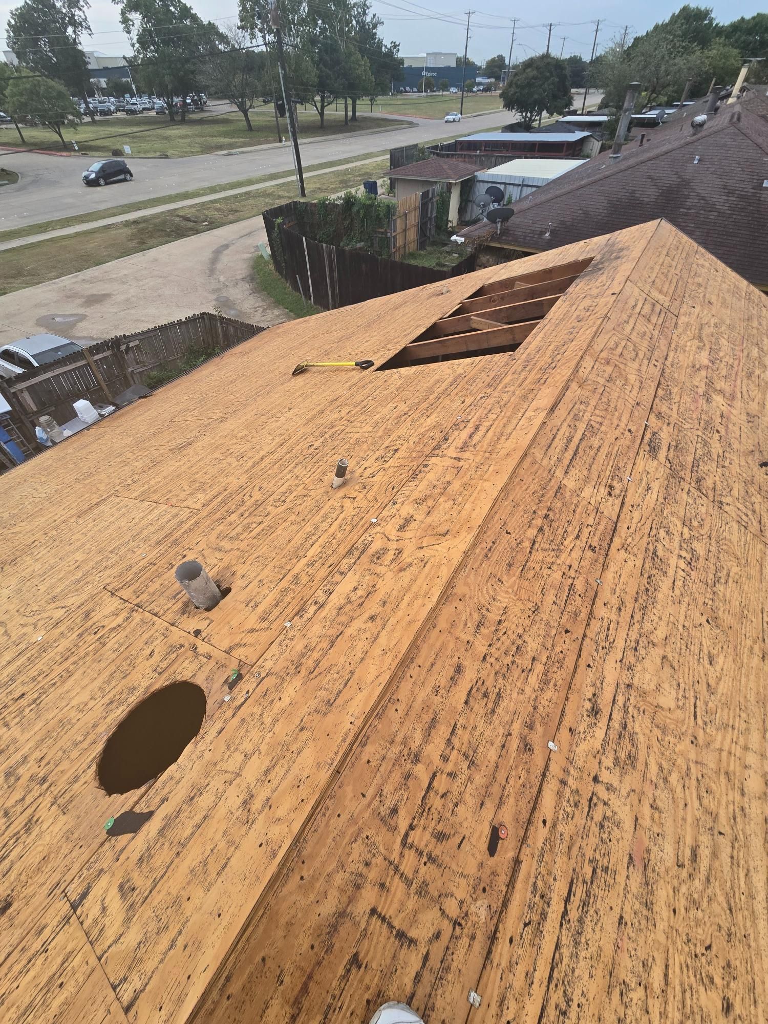 Wooden roof with a large opening, vents, and street view in the background.