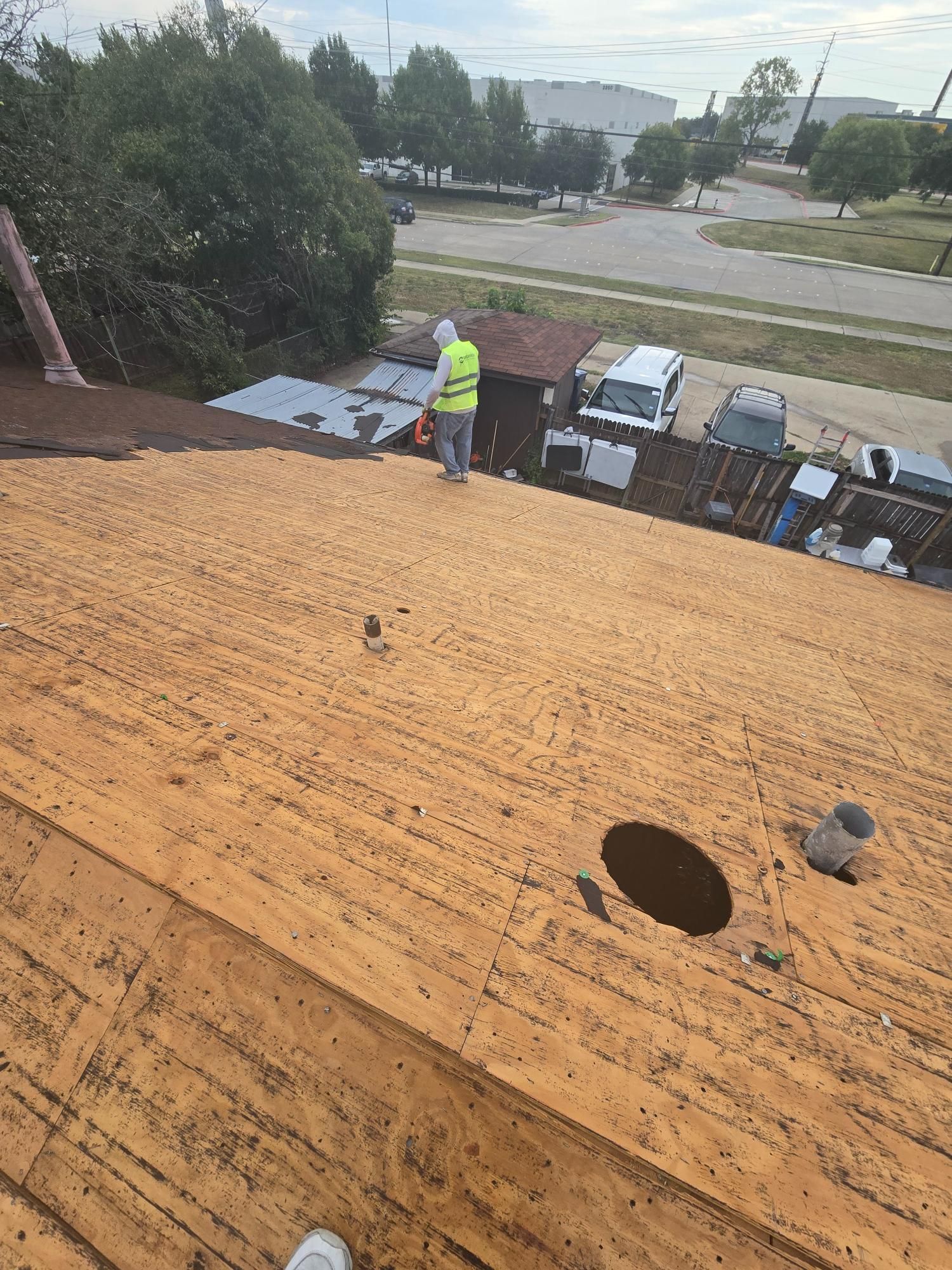 Person in safety vest on a roof, inspecting. Buildings and vehicles in the background.