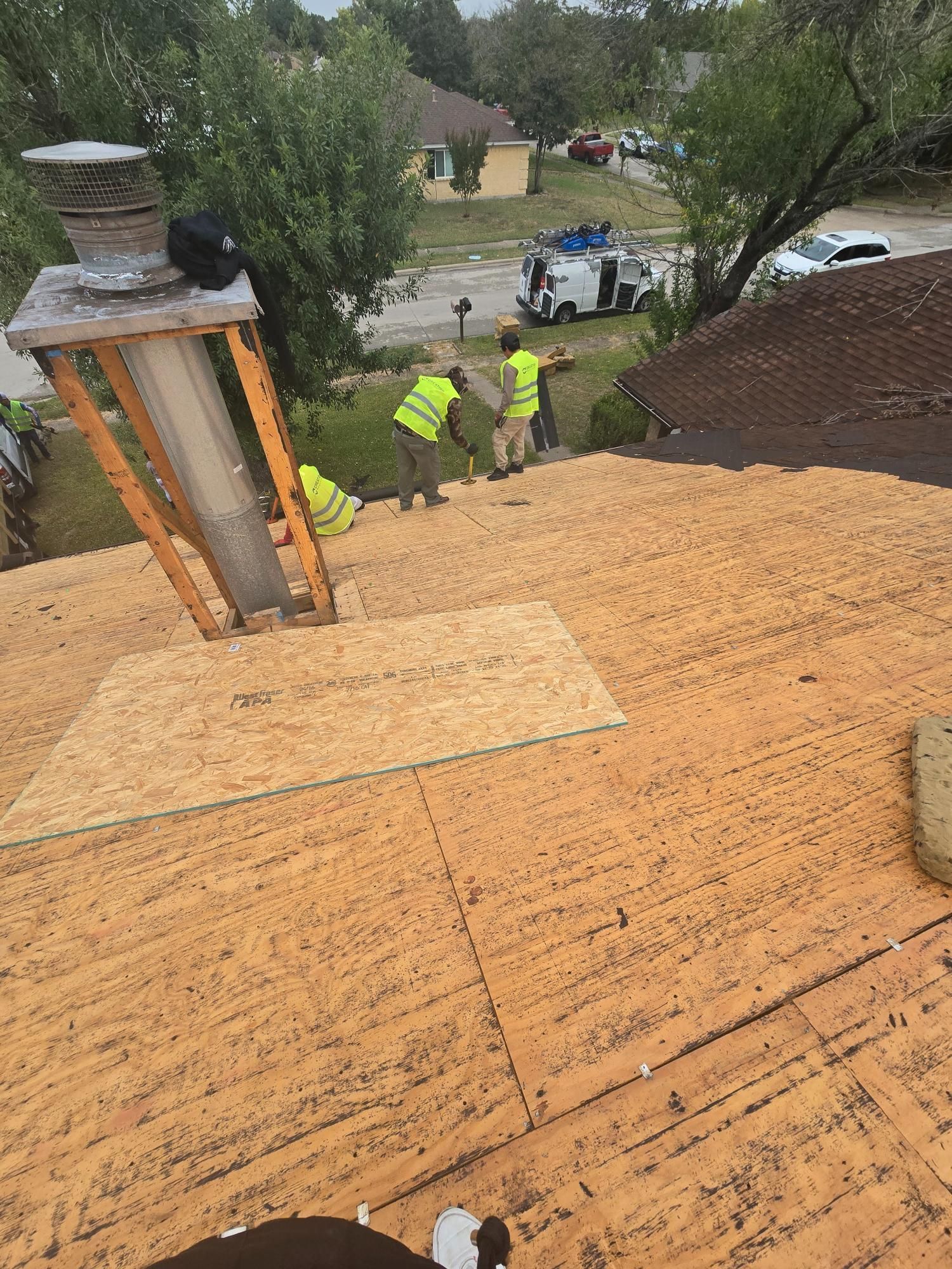 Roofers wearing safety vests working on a roof, installing new wood panels.