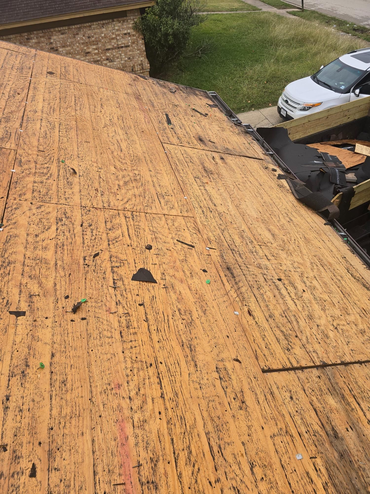 Close-up of a wood roof deck with exposed plywood. Some areas show missing pieces and wear.