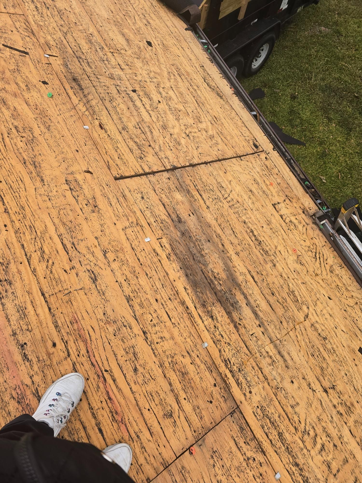 View from above of a worn wooden roof with dark streaks and a person's foot in white sneakers.