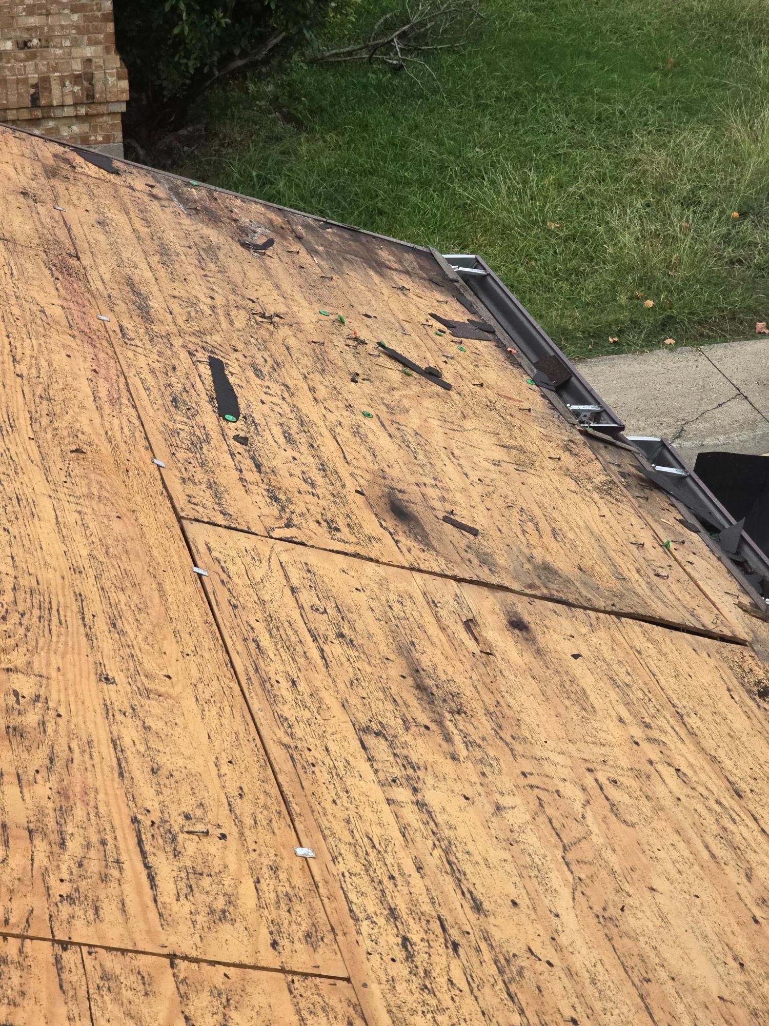 Rooftop with exposed wooden planks and a brick chimney, with green grass visible in the background.
