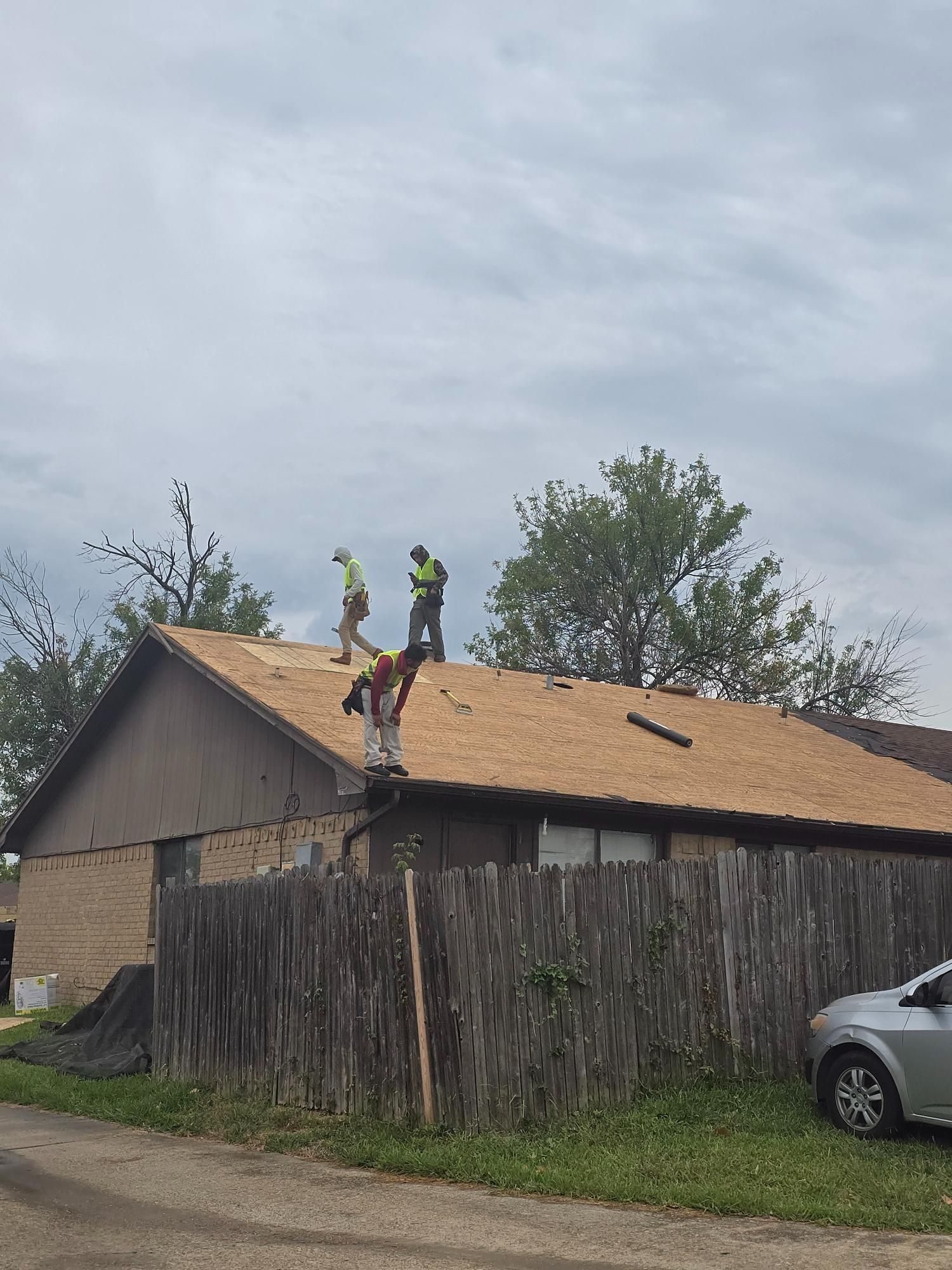 Roofers working on a residential roof, wearing safety vests. Overcast sky.