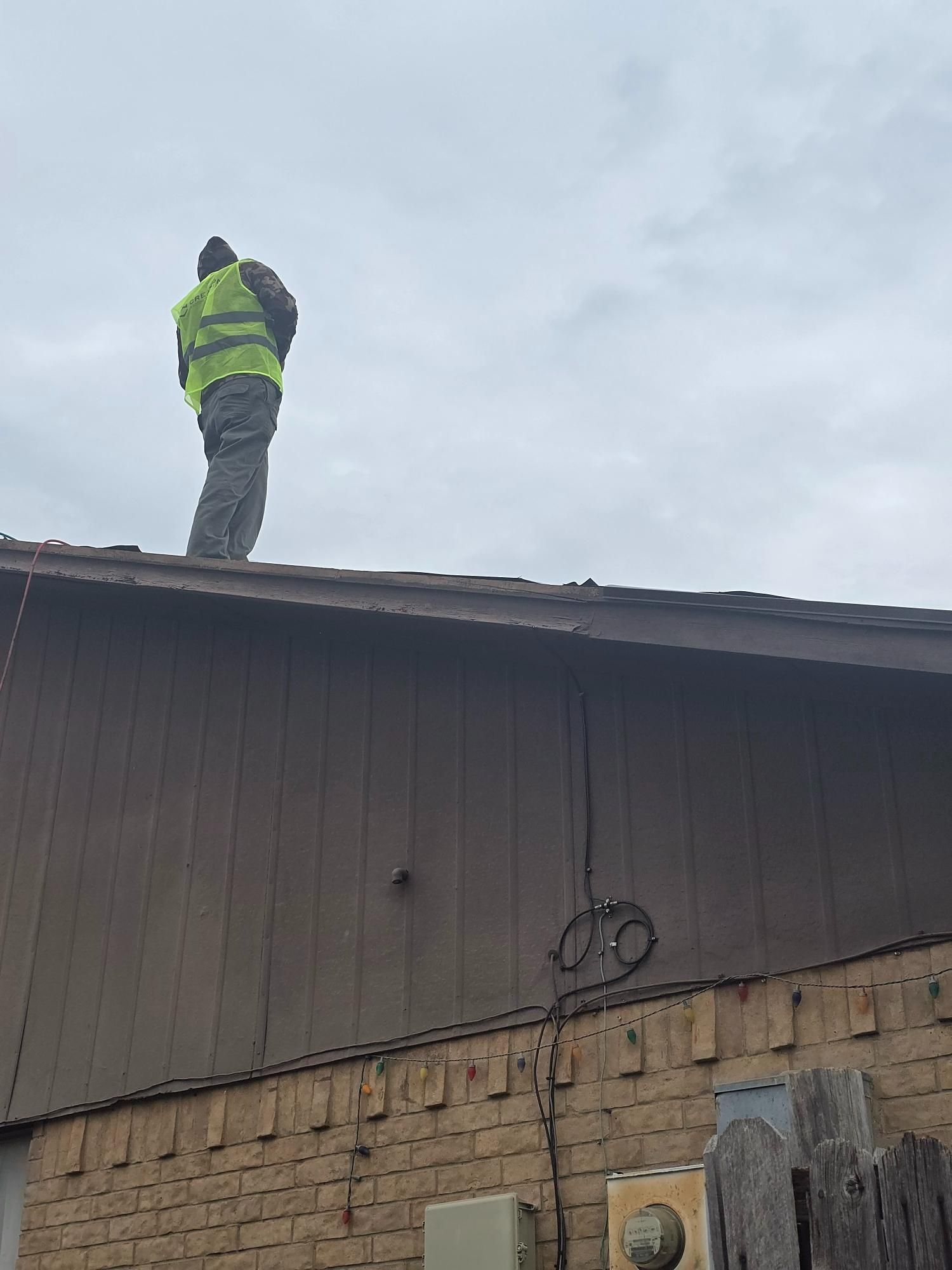 Person in yellow vest on a rooftop, inspecting or working. Cloudy sky above.