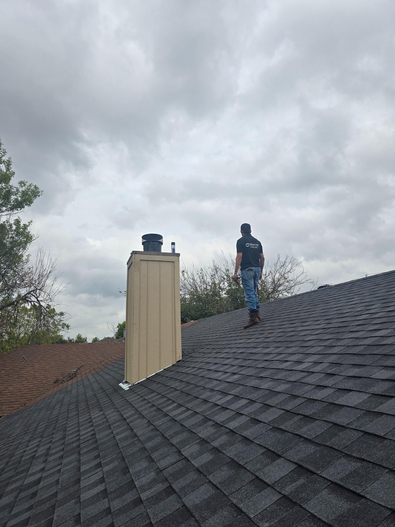 Person walks on a dark shingle roof toward a chimney with a black cap; cloudy sky overhead.