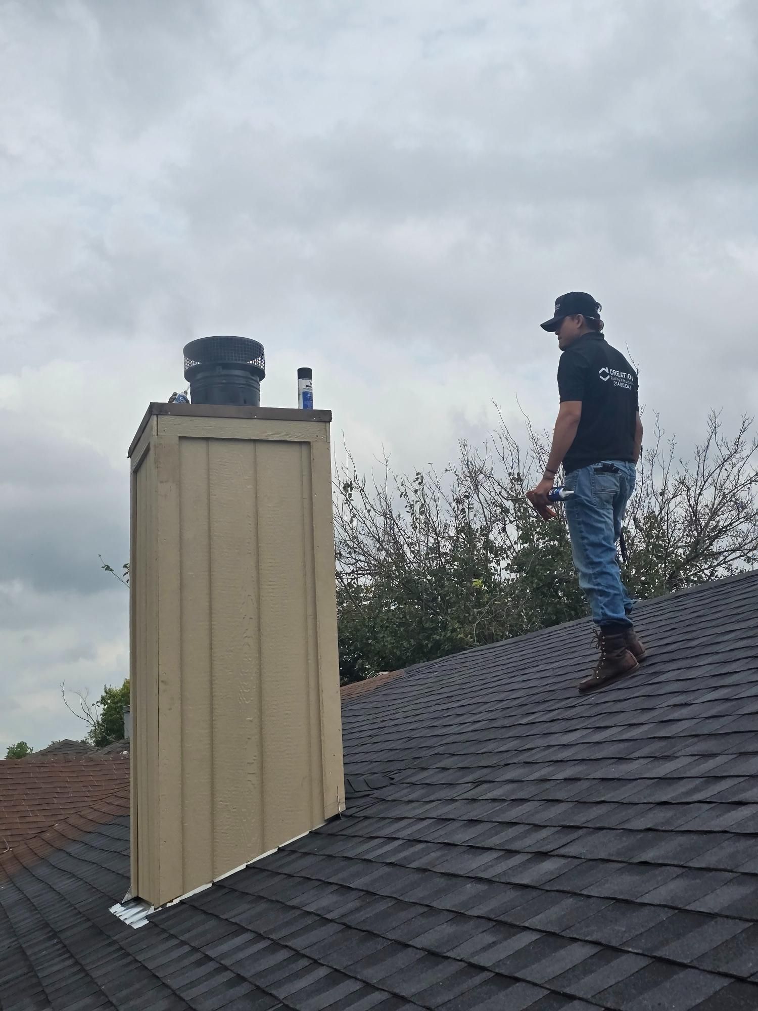 Person on a roof near a chimney, wearing jeans, looking at the chimney, overcast sky.