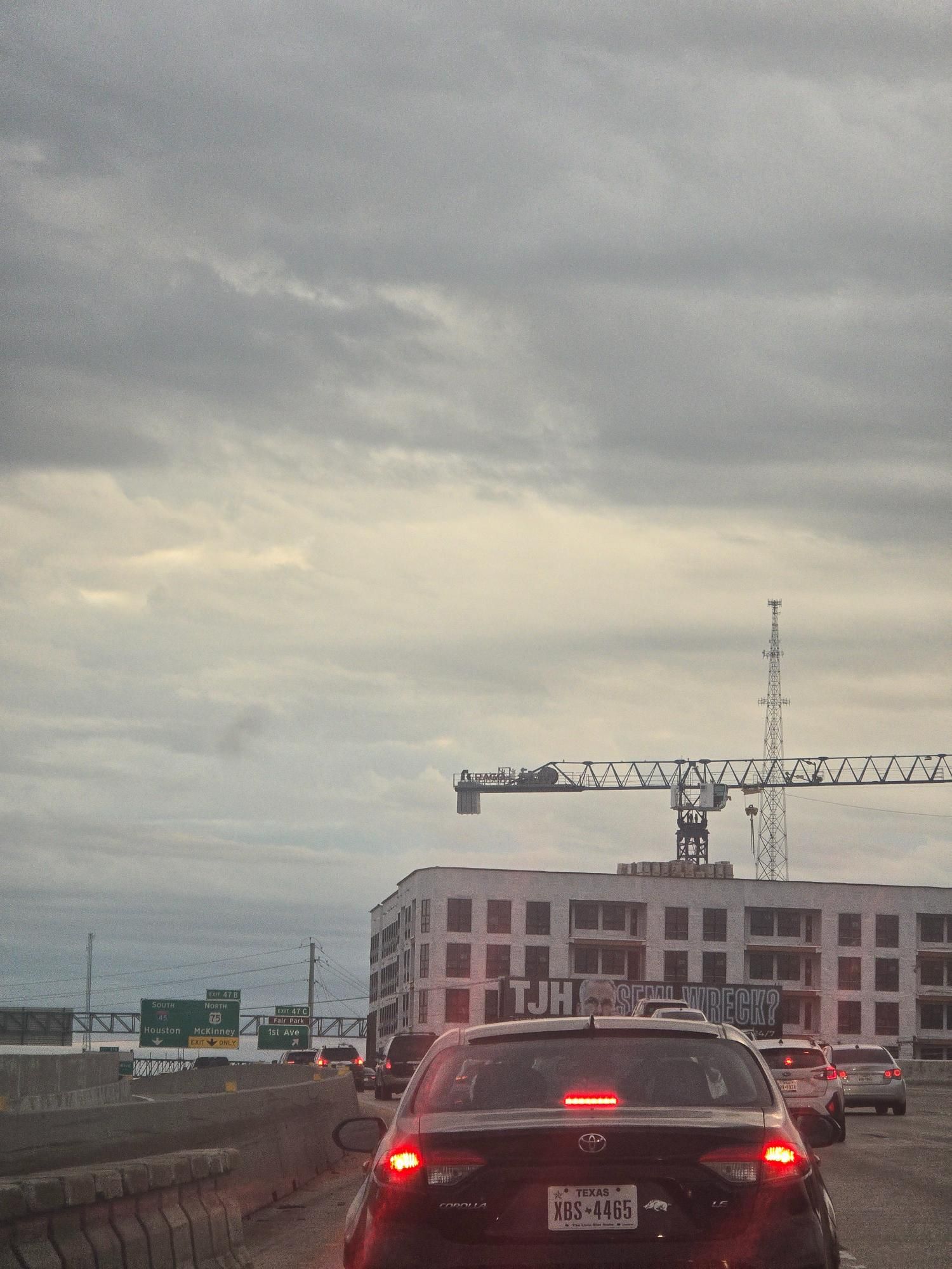 Cars on highway, passing construction site under cloudy sky.