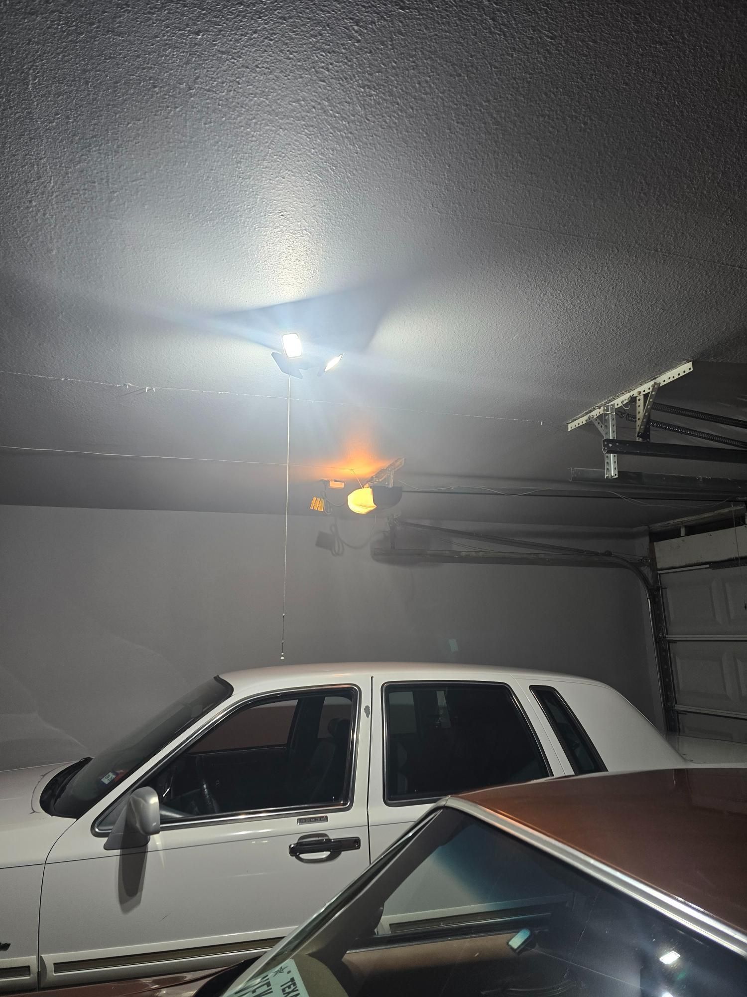 White car parked in a garage with ceiling fan and other vehicles visible.