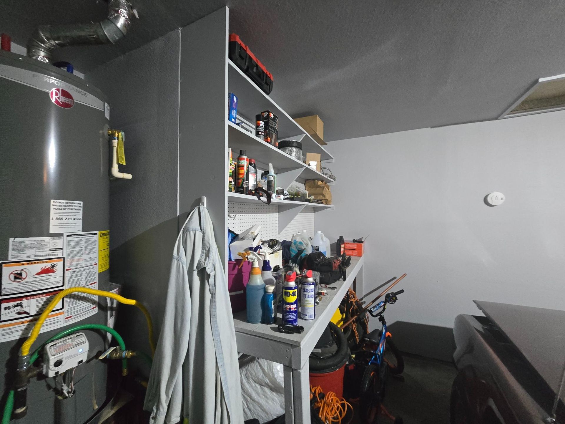 Garage interior with water heater, storage shelves, workbench, and car partially visible.