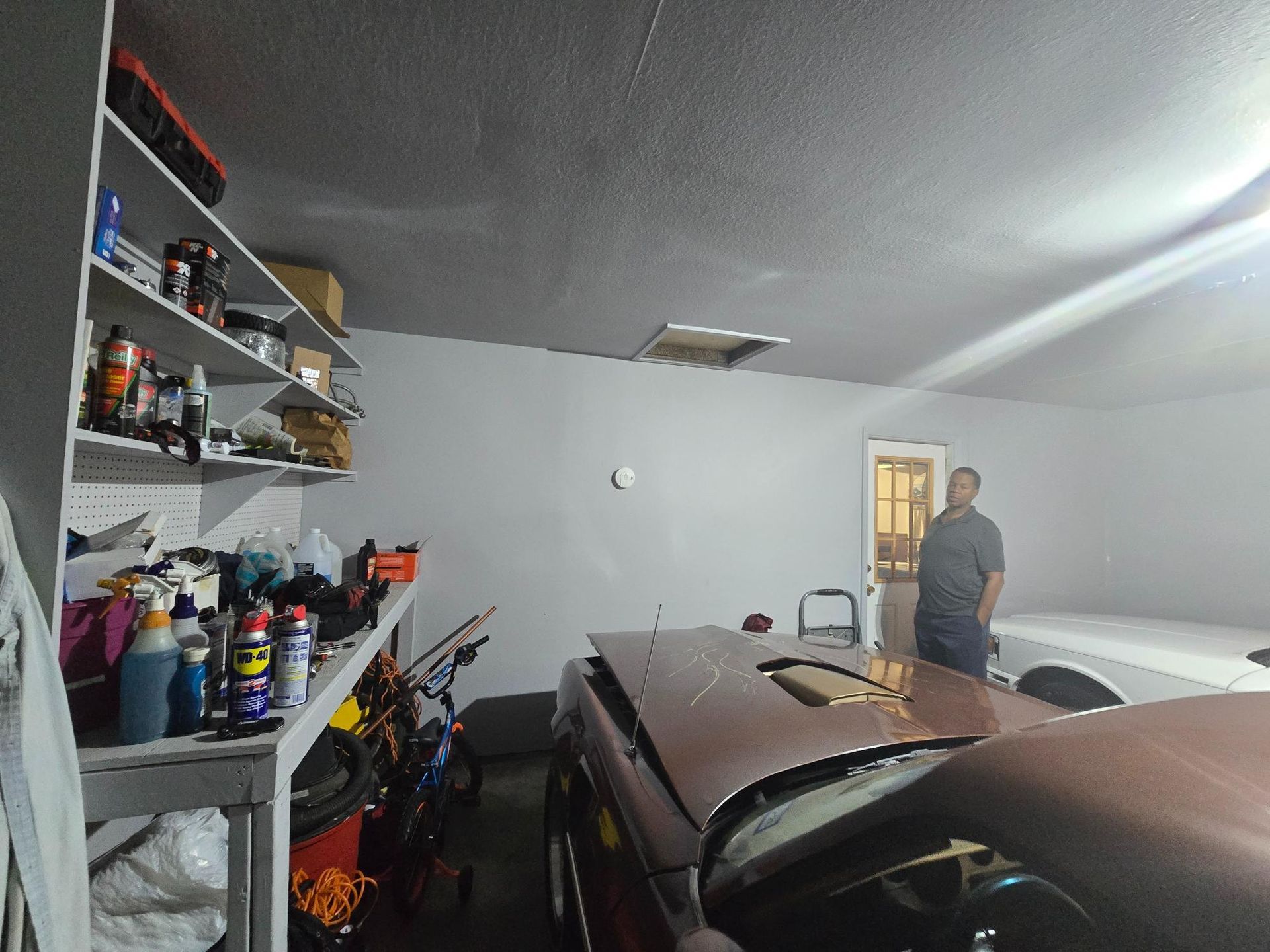 Garage interior with car, shelves of tools, and a man standing near a doorway.