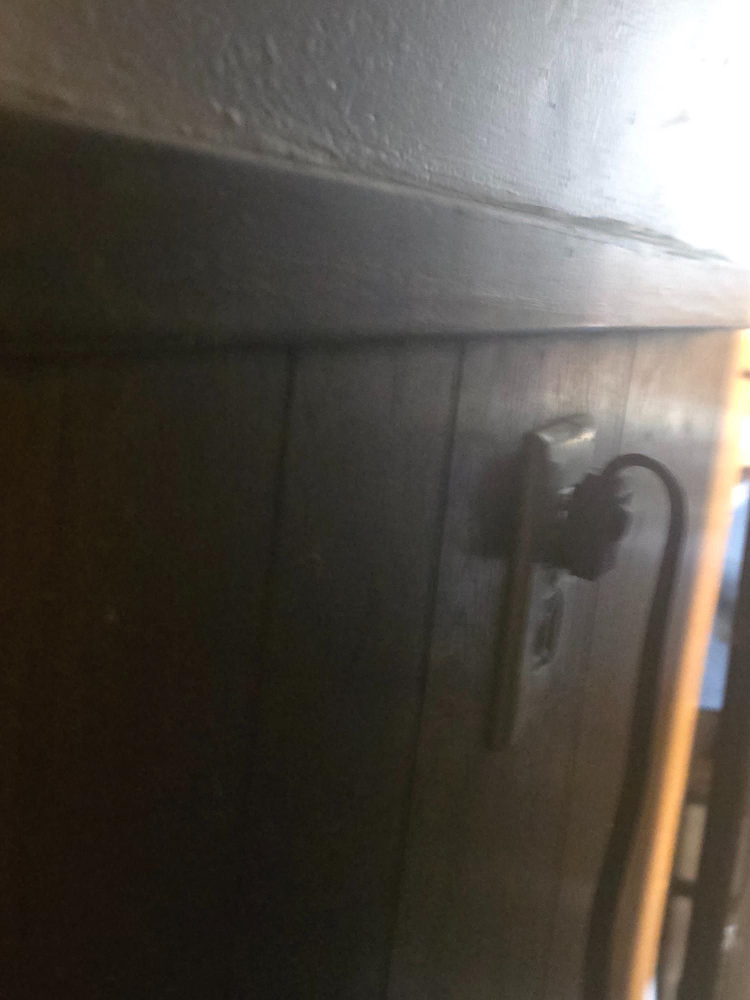 An electrical outlet with a plugged-in cord on a dark wooden surface.