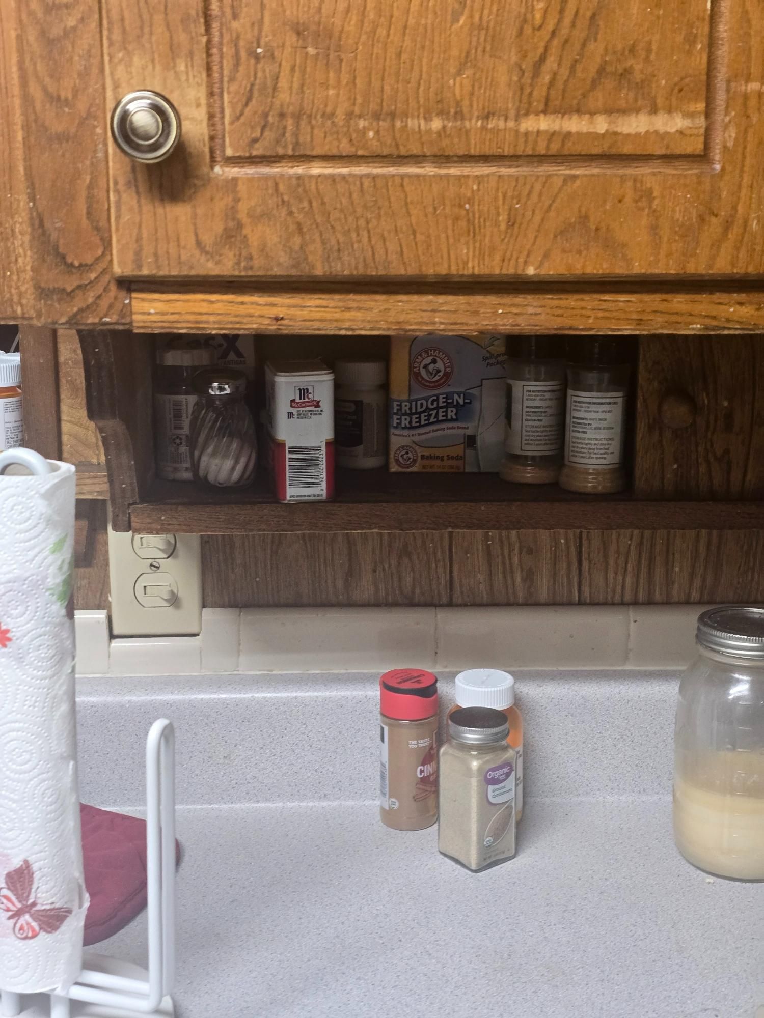 Kitchen cabinet with spices on a shelf, including a box of baking soda, and bottles on a countertop.