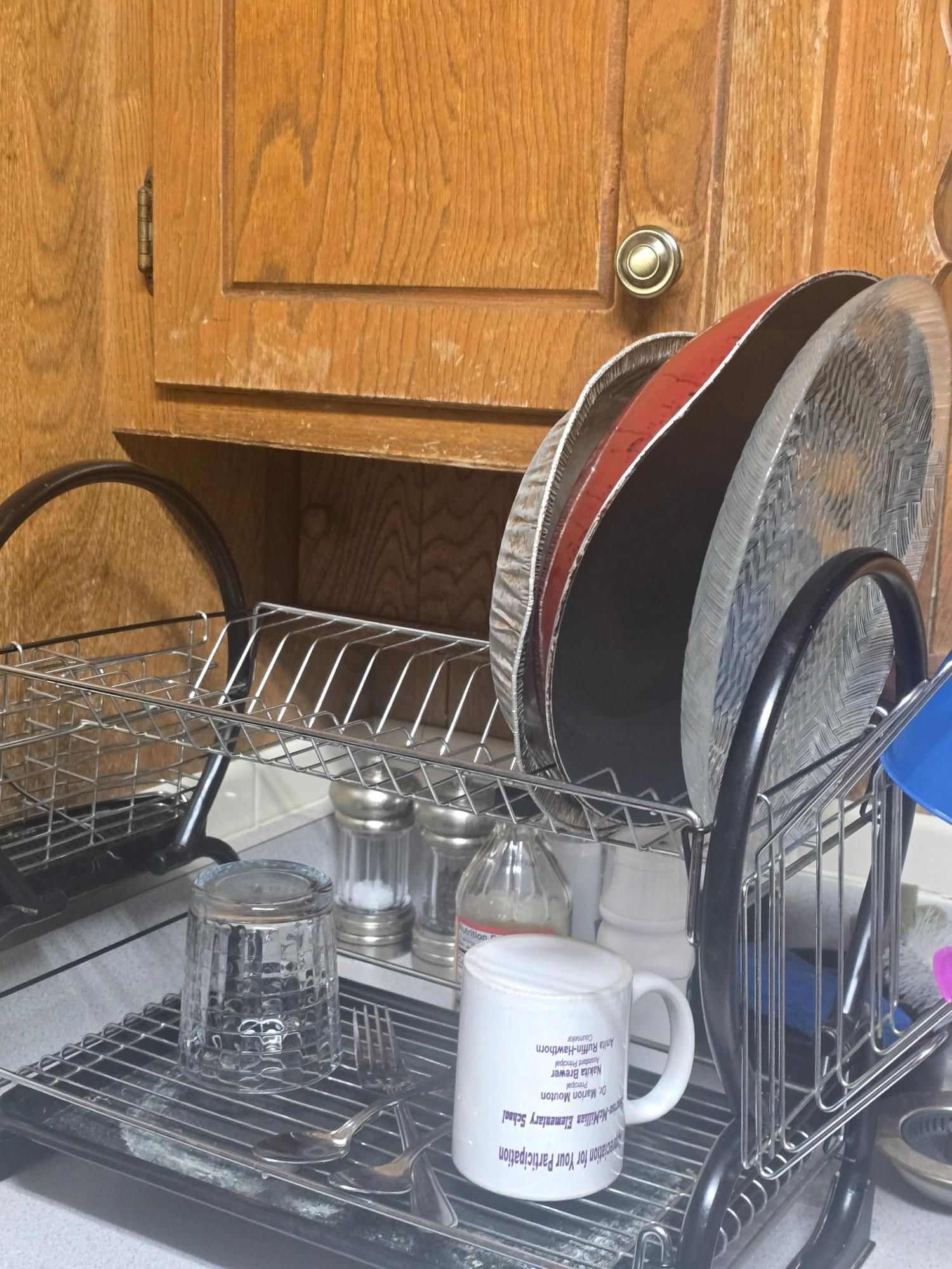 Dishes drying in a rack under a wooden cabinet, including plates, glasses, and a mug.