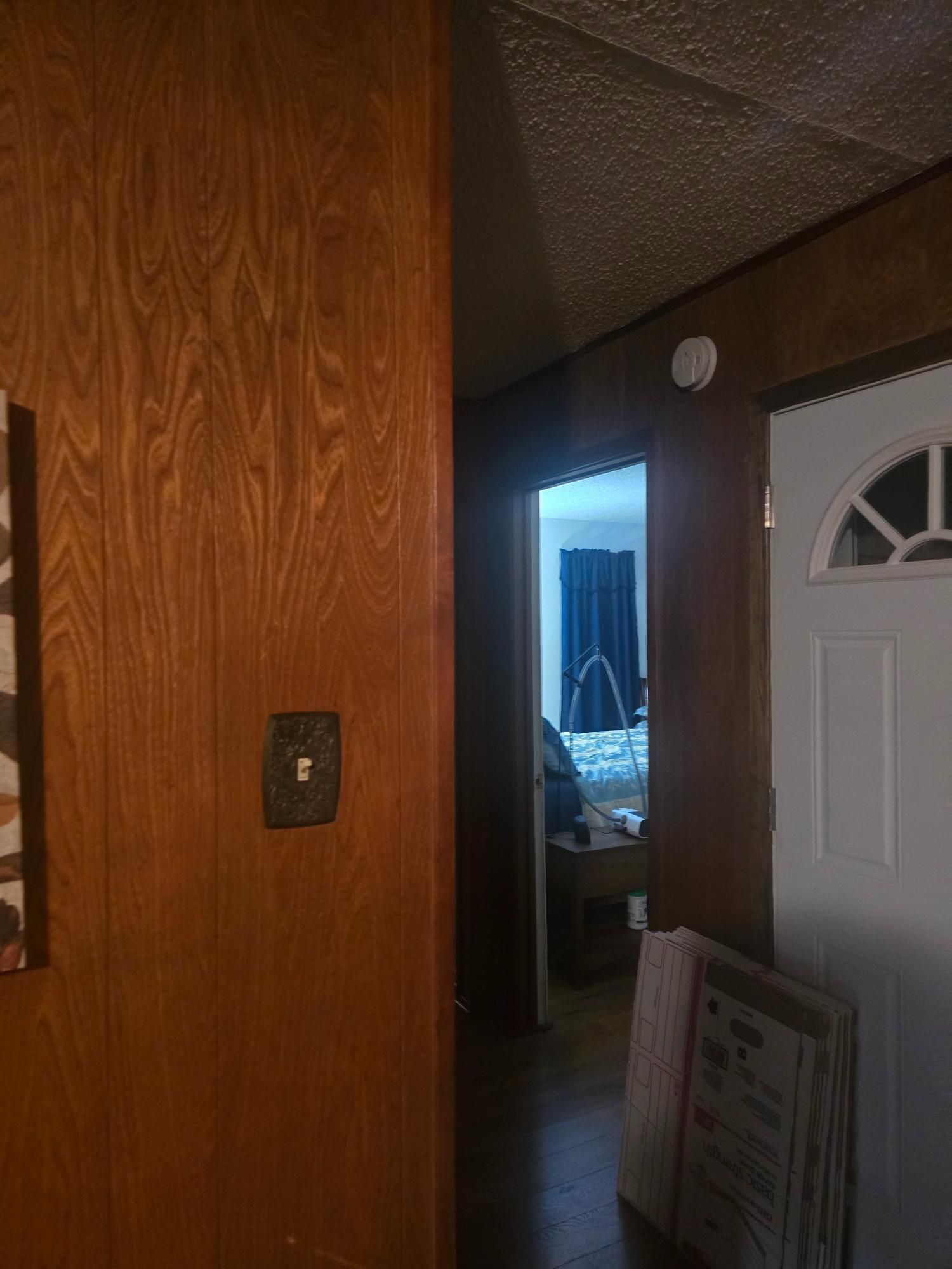 Hallway with wood paneling, open doorway to bedroom, and white front door with arched window.