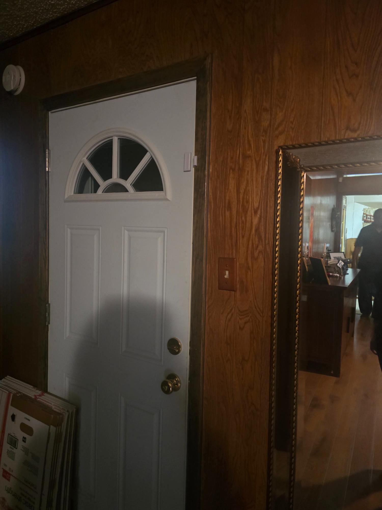 White door with arched window, framed by wood paneling; mirror on right reflecting interior.