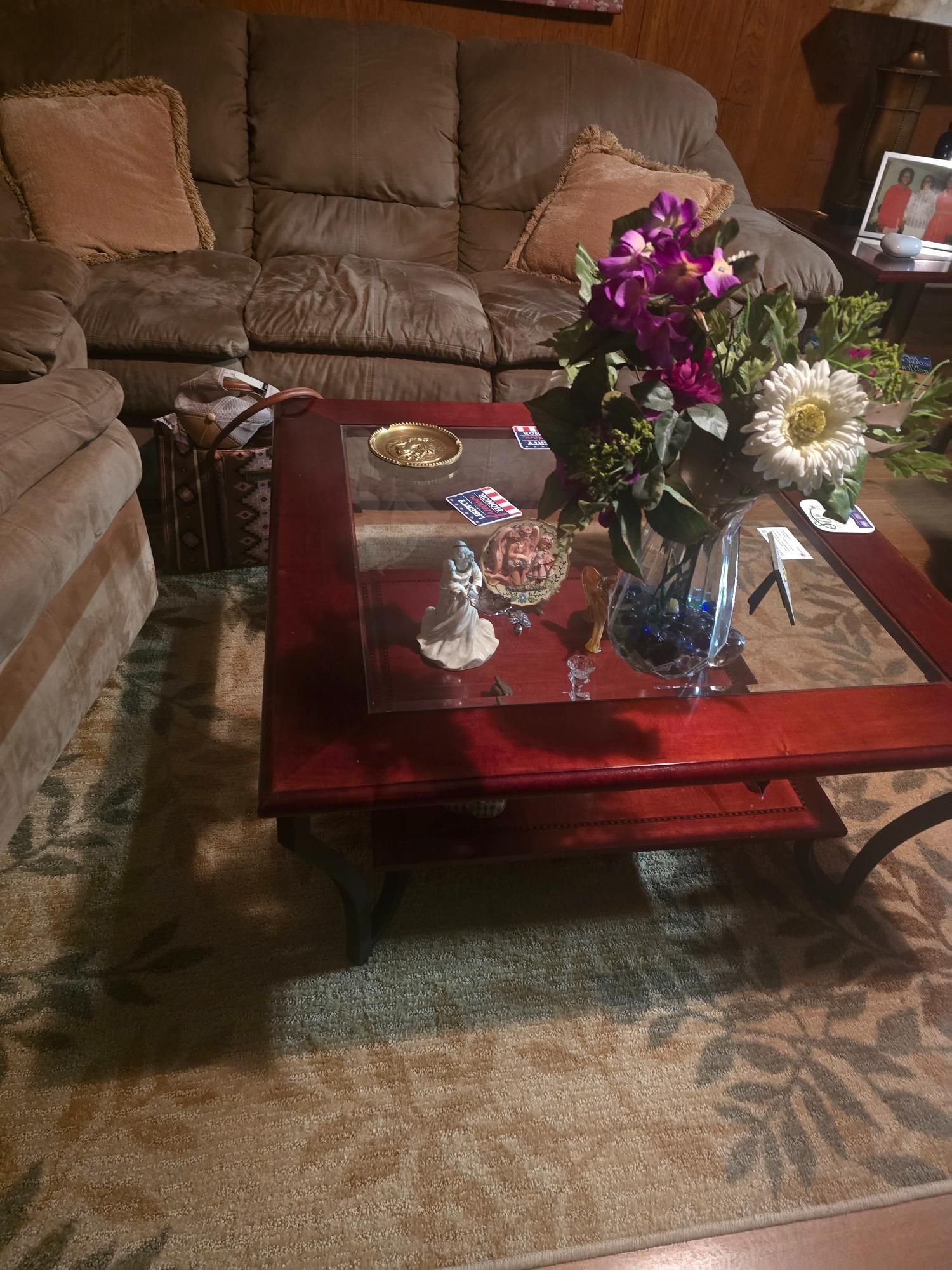 Living room with a brown couch, a coffee table, and a rug with floral patterns. Flowers sit on the table.