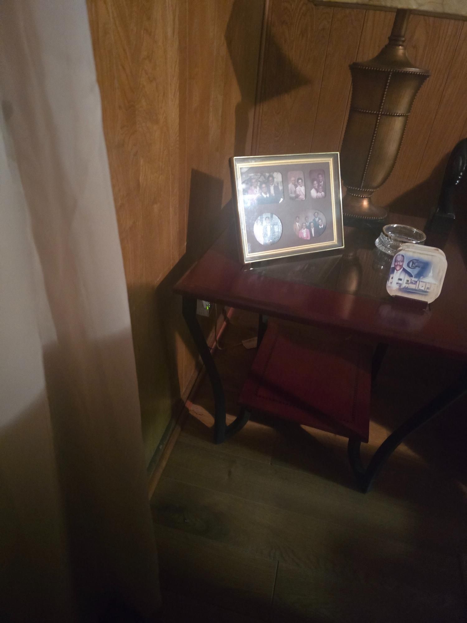 Dark corner with a red table holding a framed photo, a lamp, and a tissue box.