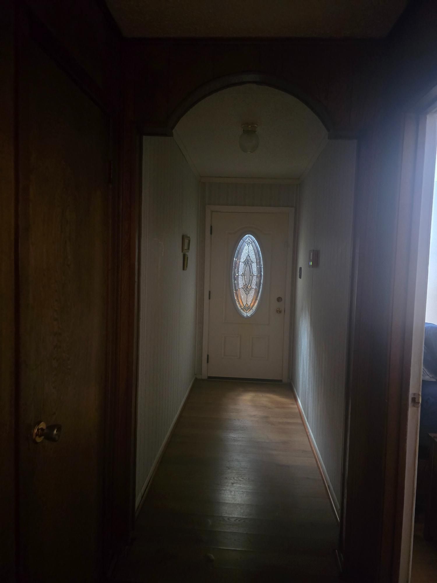 Hallway with wooden floor, white walls, and a front door with an oval glass window.
