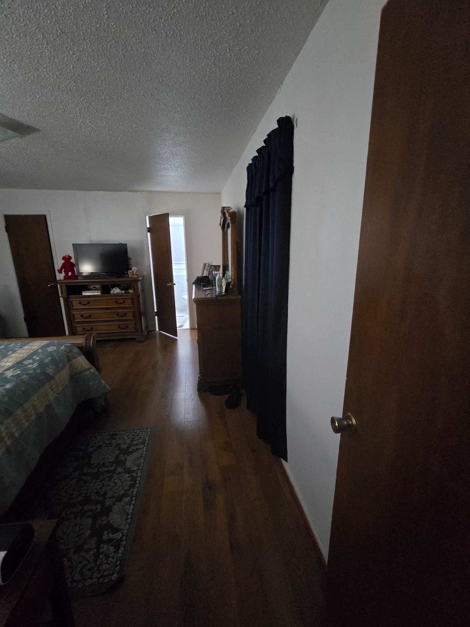 Bedroom interior with bed, TV on dresser, and closed doors. Dark curtains on wall.