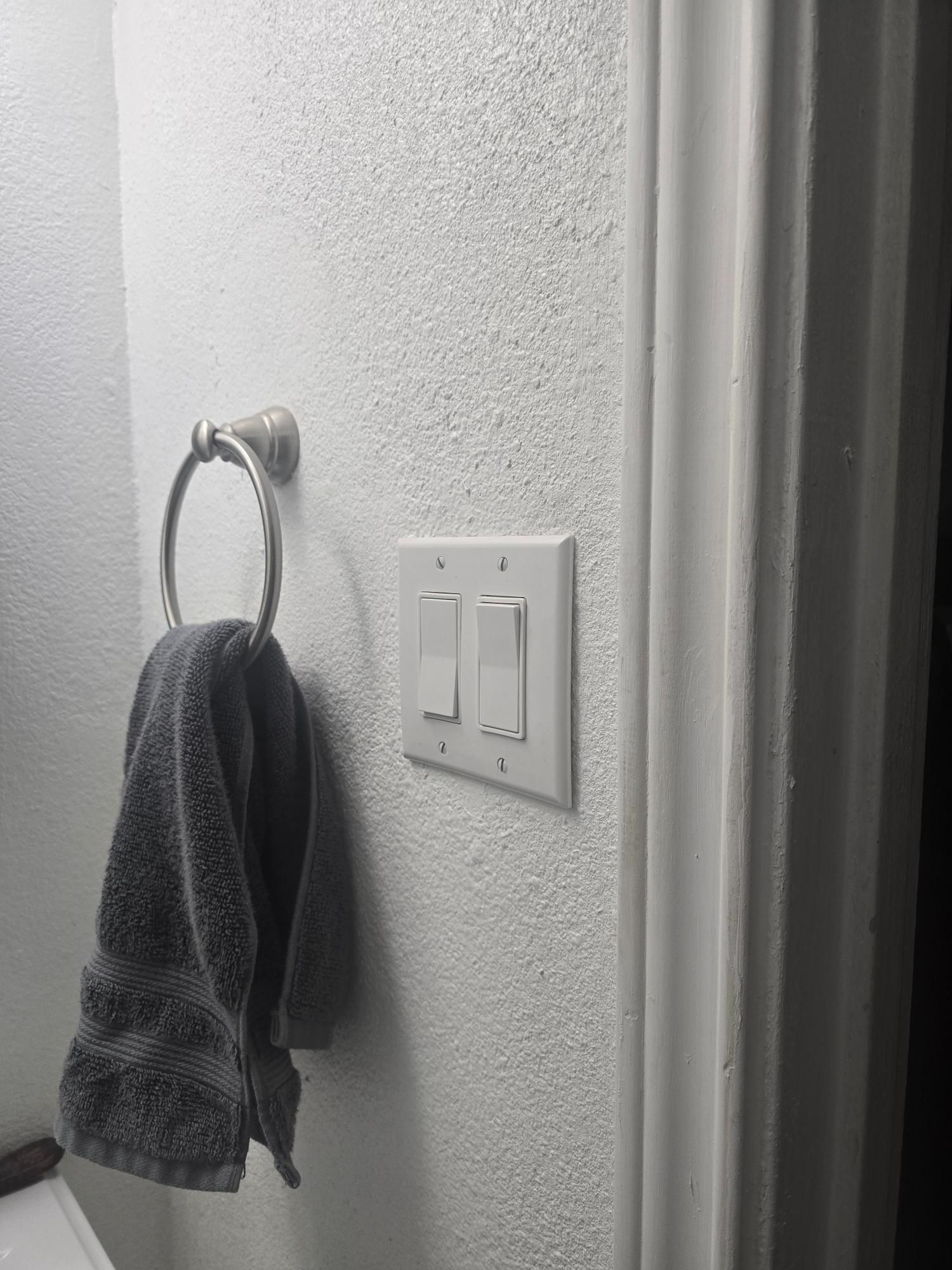 Towel on a ring next to a light switch plate on a textured white wall in a bathroom.