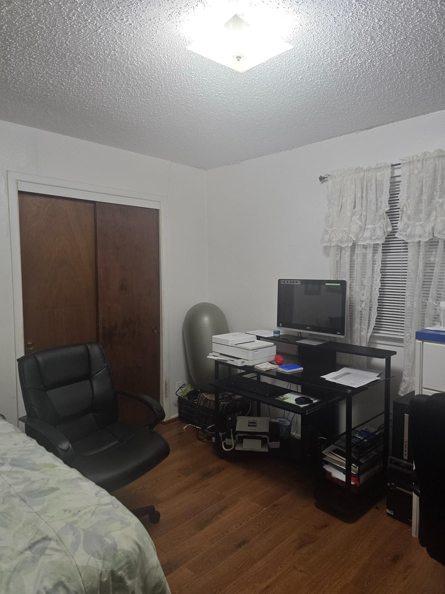 A room with a bed, desk, chair, closet and window with blinds and curtains.