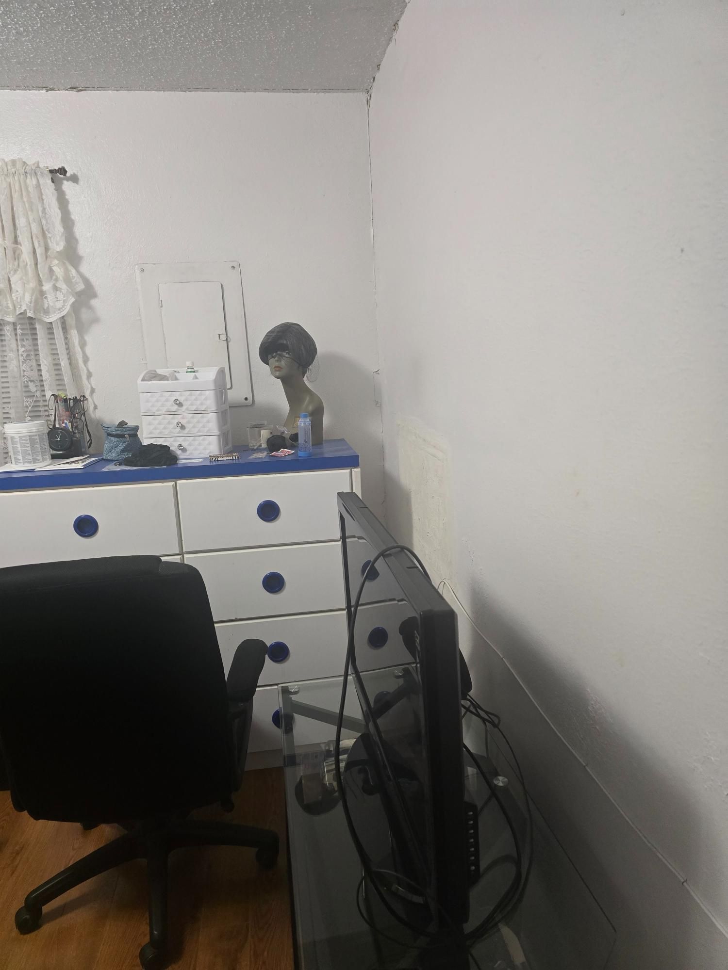 A black office chair next to a white dresser with blue trim and a computer monitor in a corner.