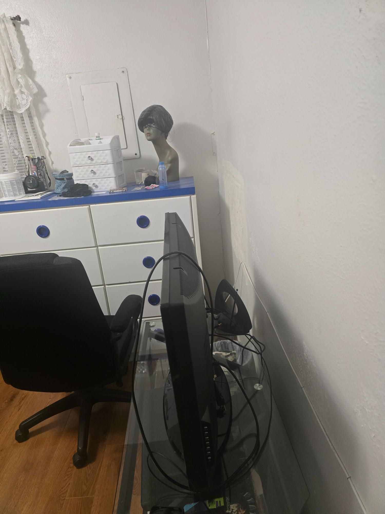 Computer monitor on a desk, office chair, dresser, mannequin head, and sewing machine.