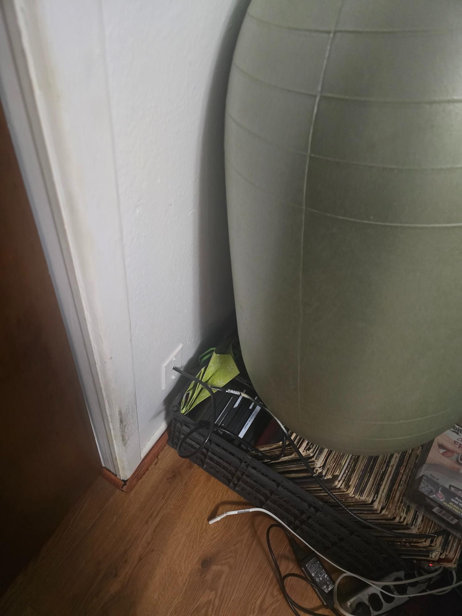 A green exercise ball sits against a white wall in a corner, over a basket and rug on a wood floor.