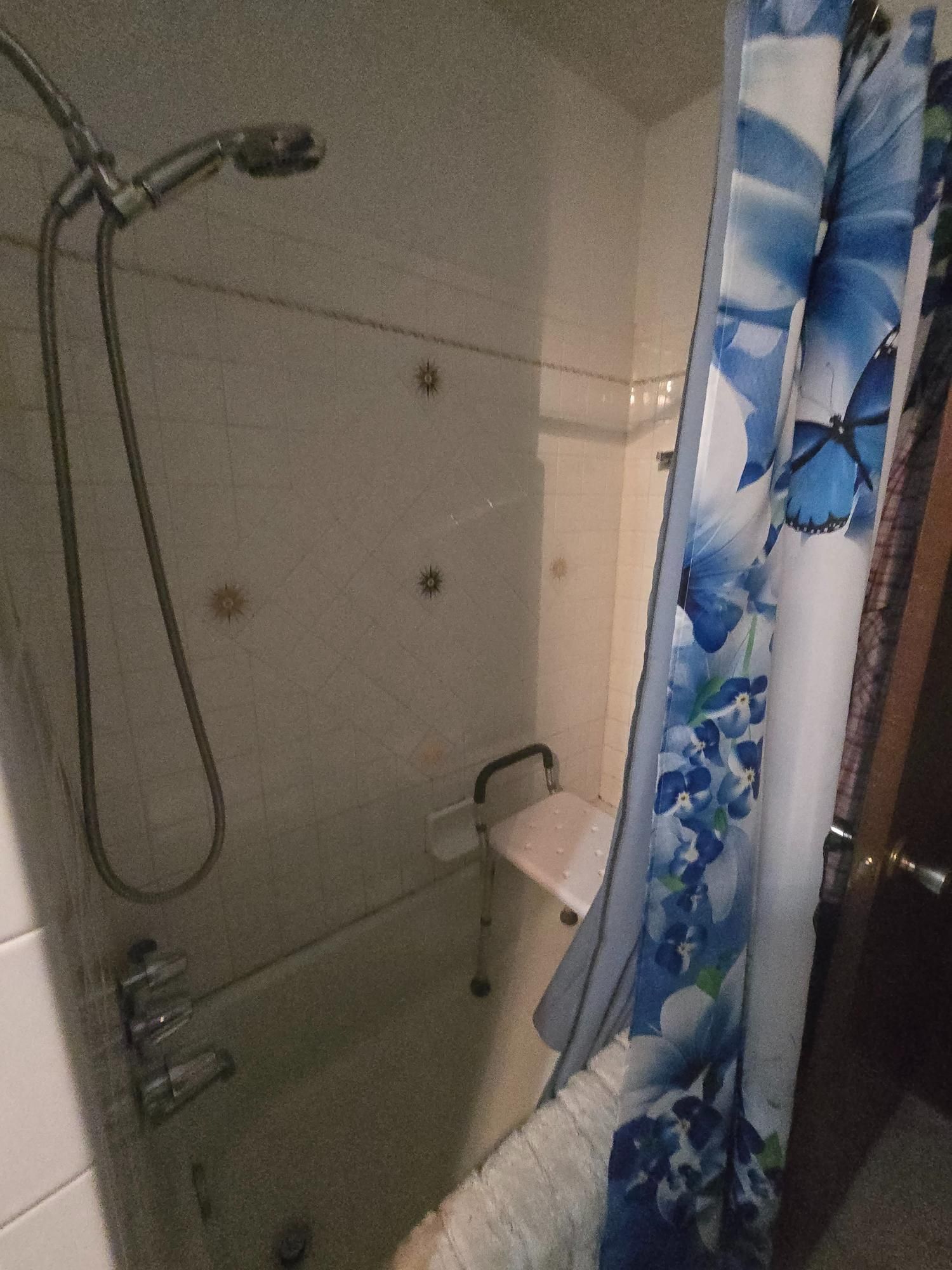 Shower stall with a shower seat, handheld showerhead, and floral shower curtain.