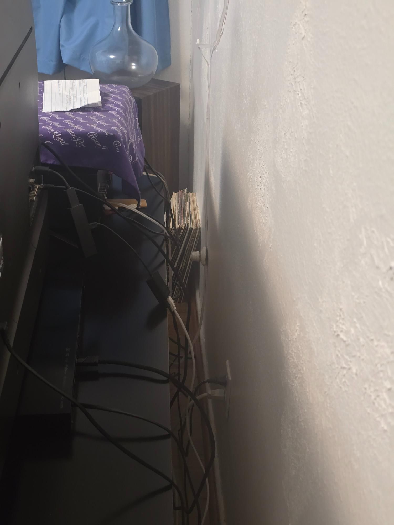 Black cabinet against a white wall with tangled cords. Purple tablecloth and glass bottle visible.