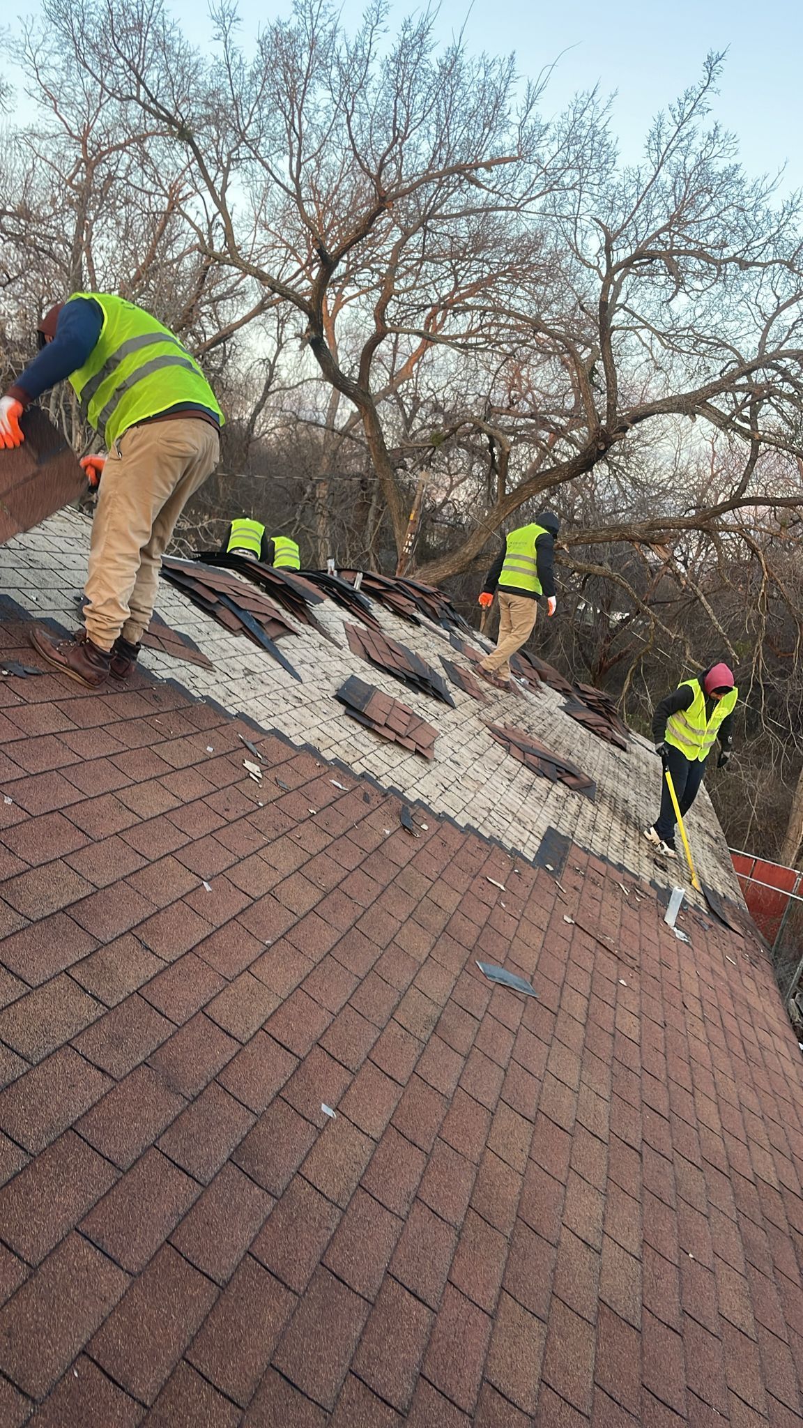 Three workers in safety vests removing old shingles from a roof.