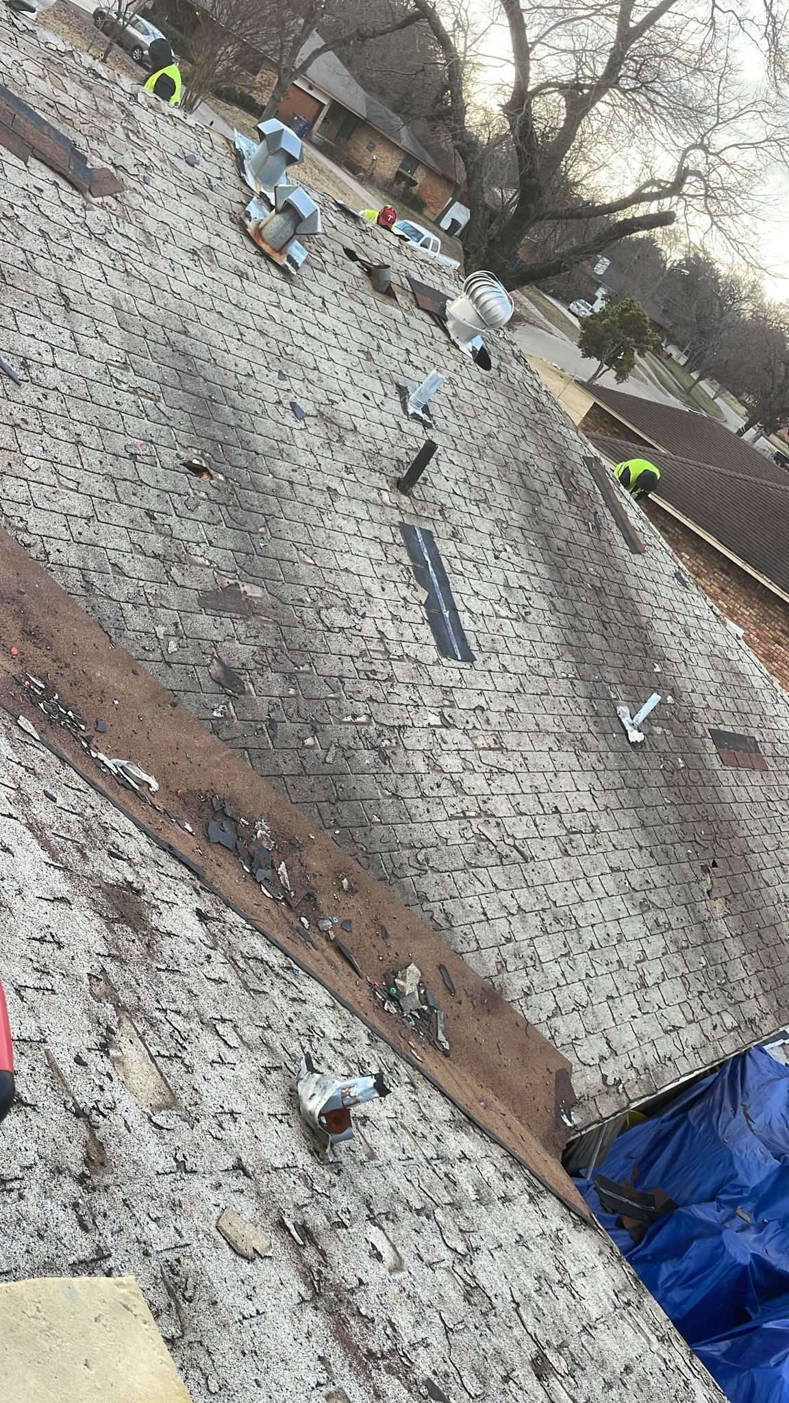 Rooftop with partial tear-off, exposing wood; tools and workers visible. Blue tarp and safety gear.