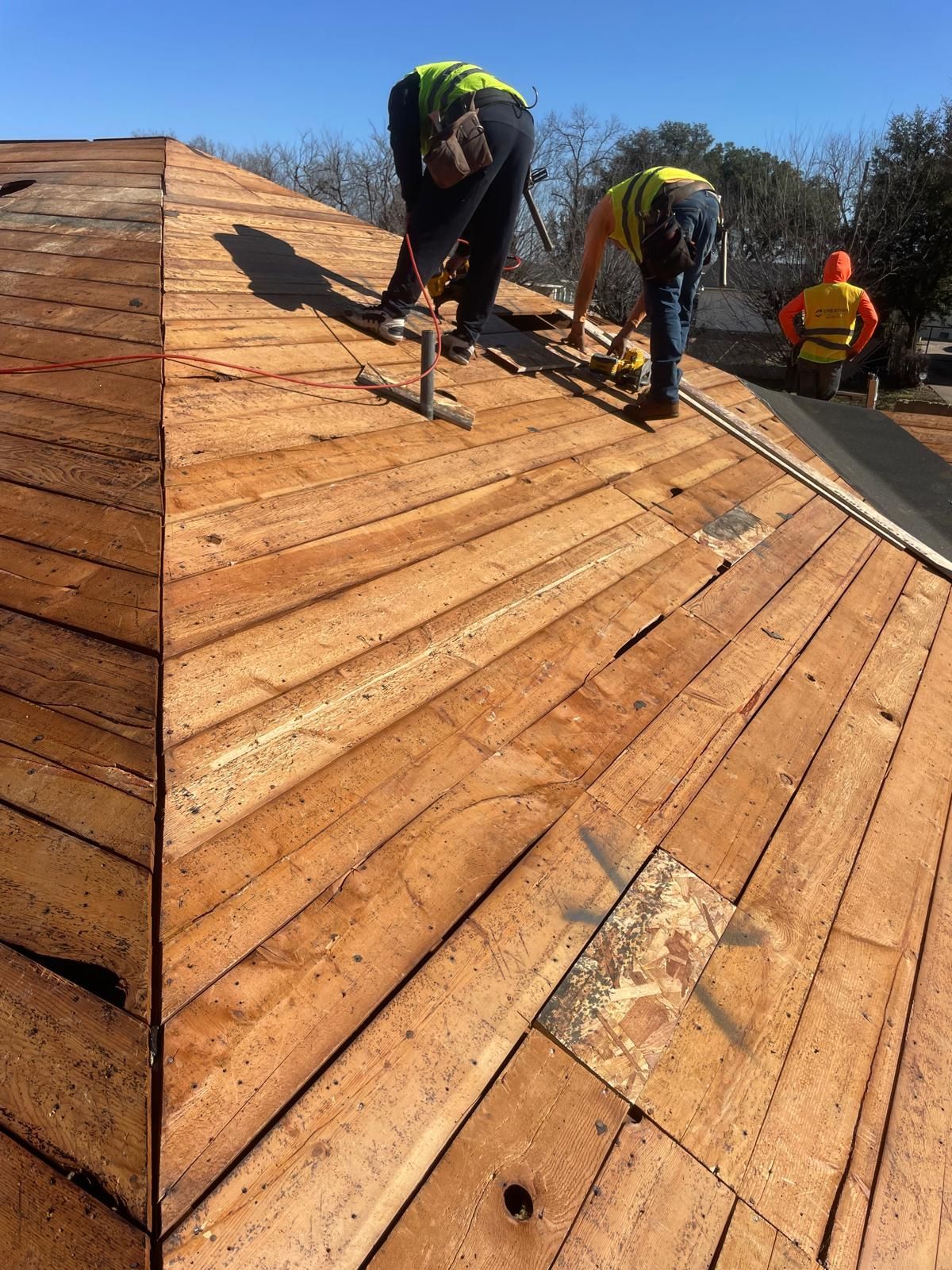 Construction workers installing shingles on a wooden roof under a bright blue sky.