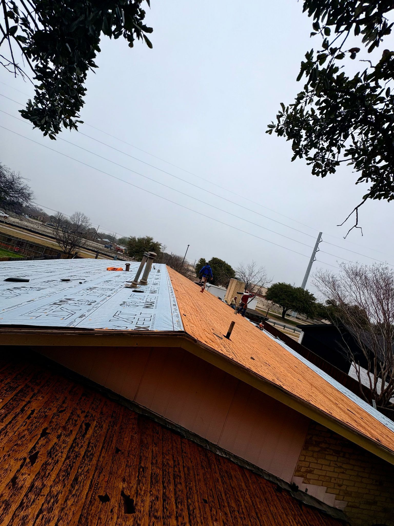 Workers on a rooftop, replacing the roof. Overcast day.