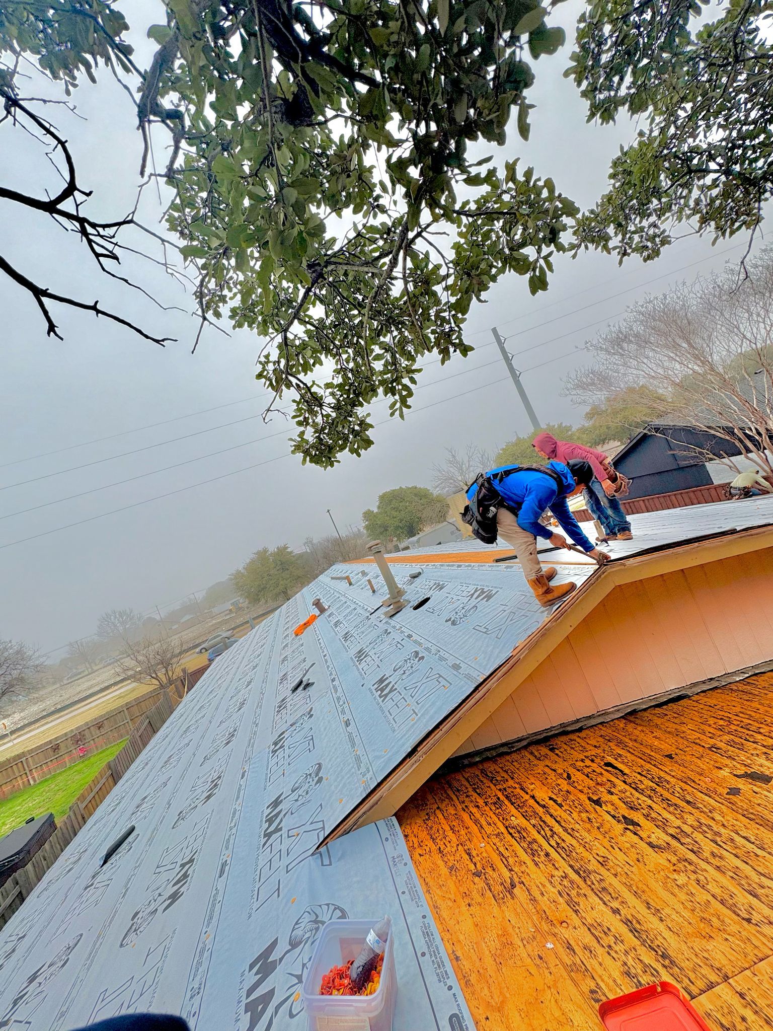 Two workers installing metal roofing on a house under a cloudy sky.