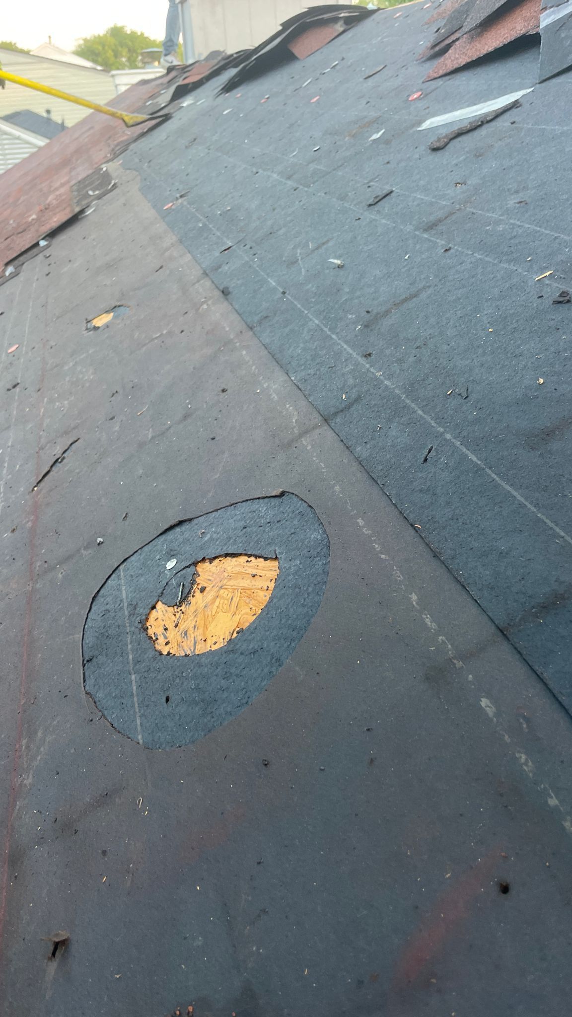 Damaged asphalt shingle roof with a large, exposed area of underlayment.